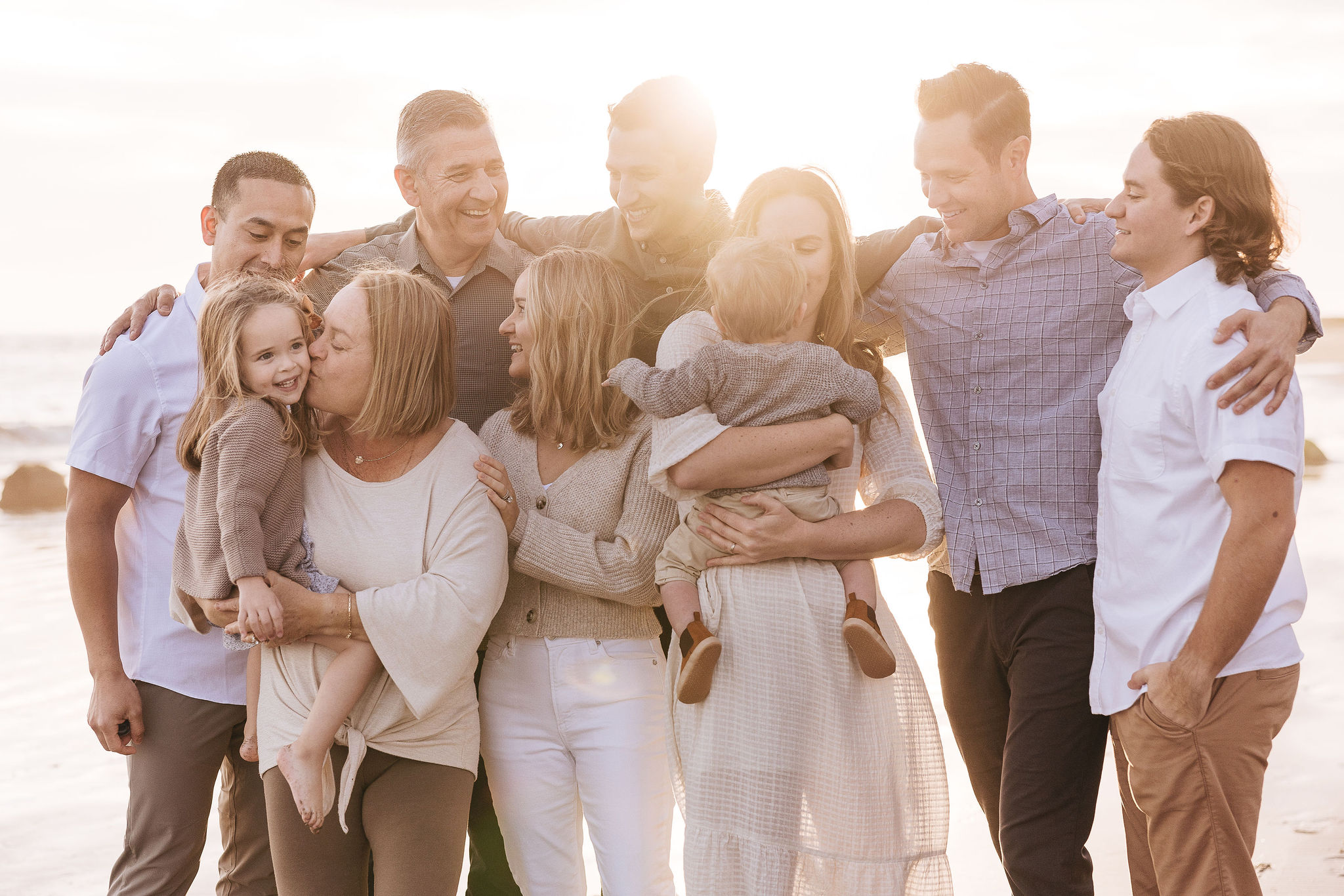 Group of adults and children hugging and smiling outdoors on a sunny day, standing close together.