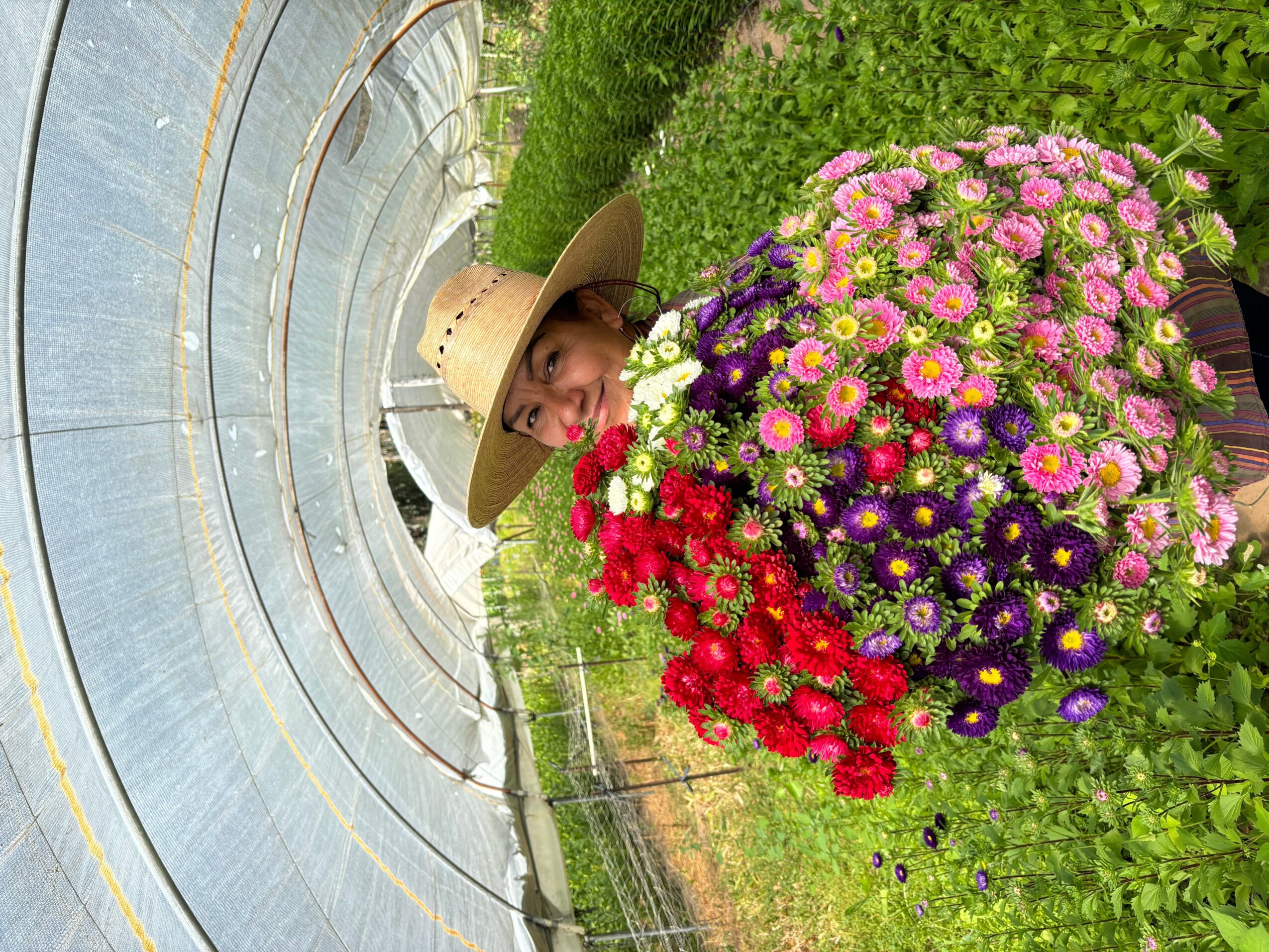 Person wearing a wide-brimmed hat standing next to a large colorful flower arrangement in a garden.