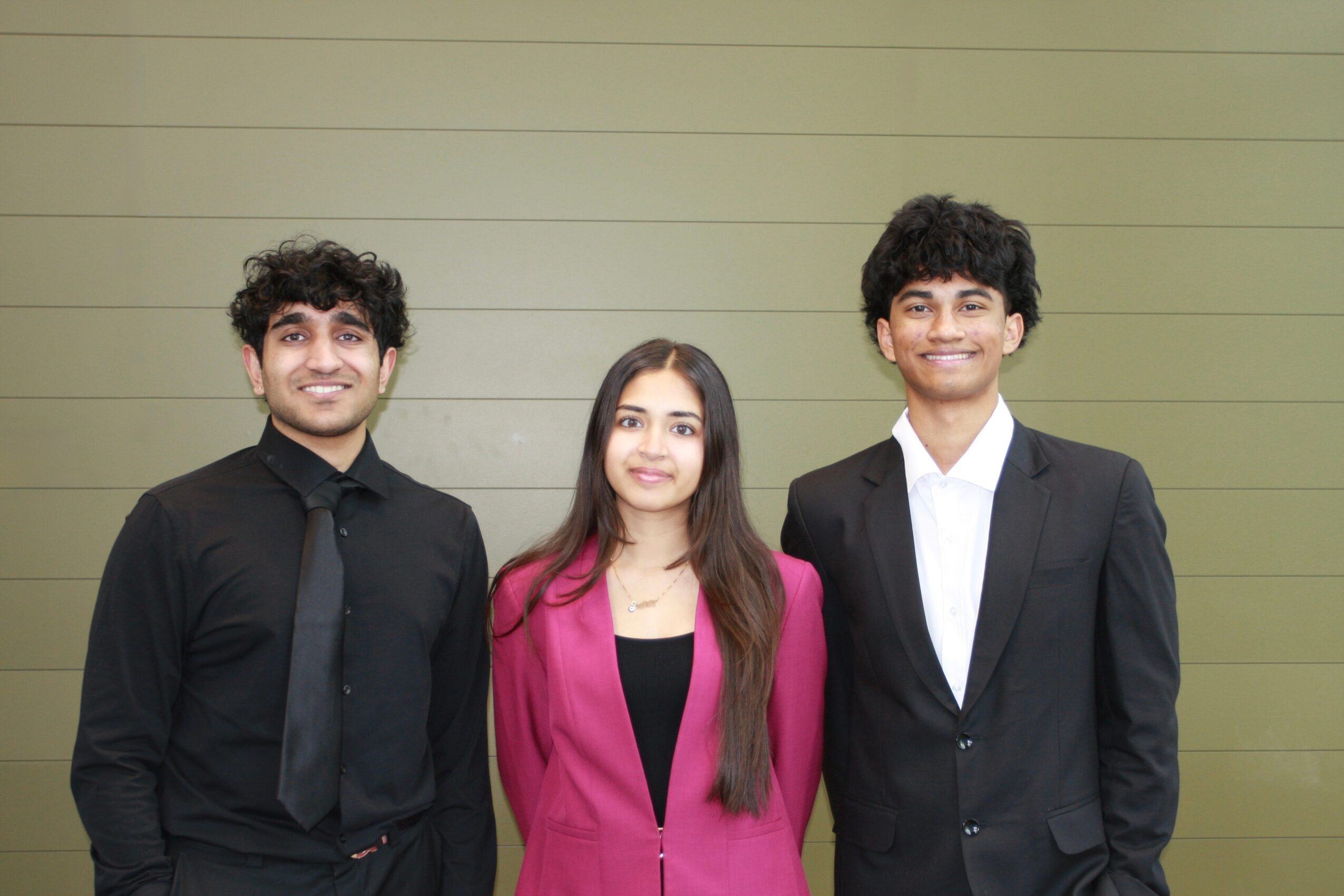 Three young people standing side by side, smiling, against a green wall background.