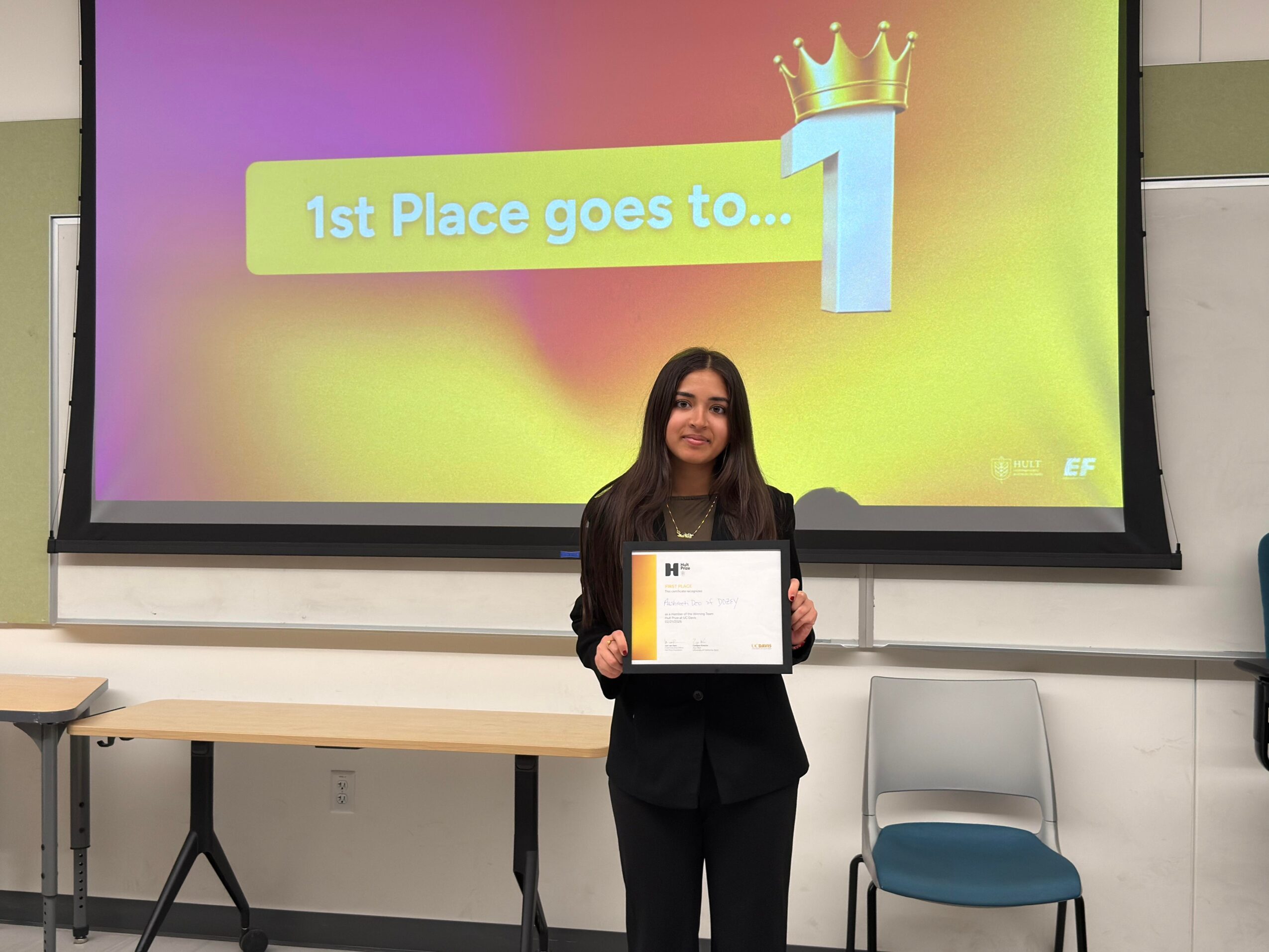 Young woman holding a certificate in front of a presentation screen with a yellow background and a crown icon.