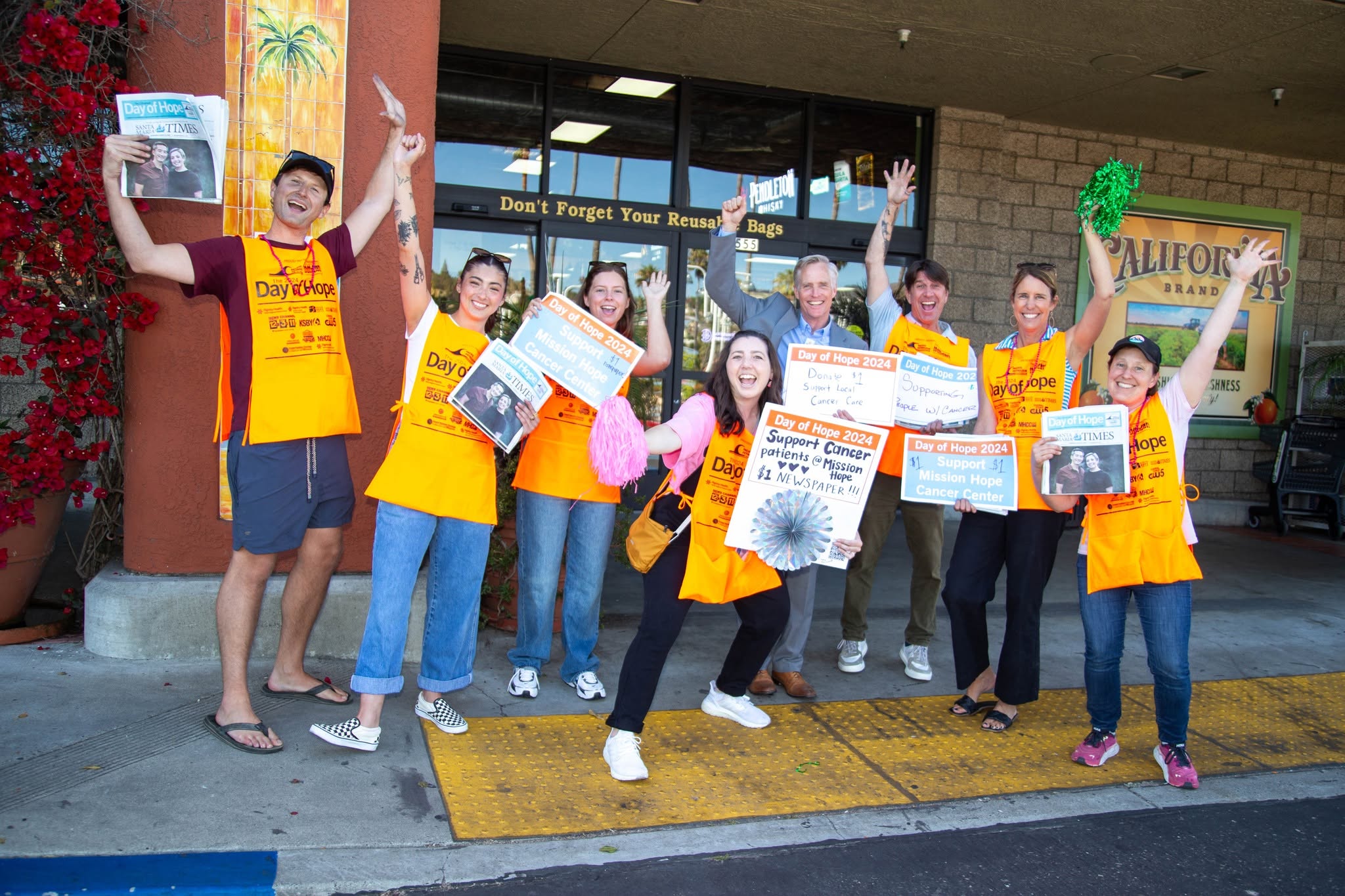 Group of people wearing yellow shirts holding signs and raising hands outside a building.