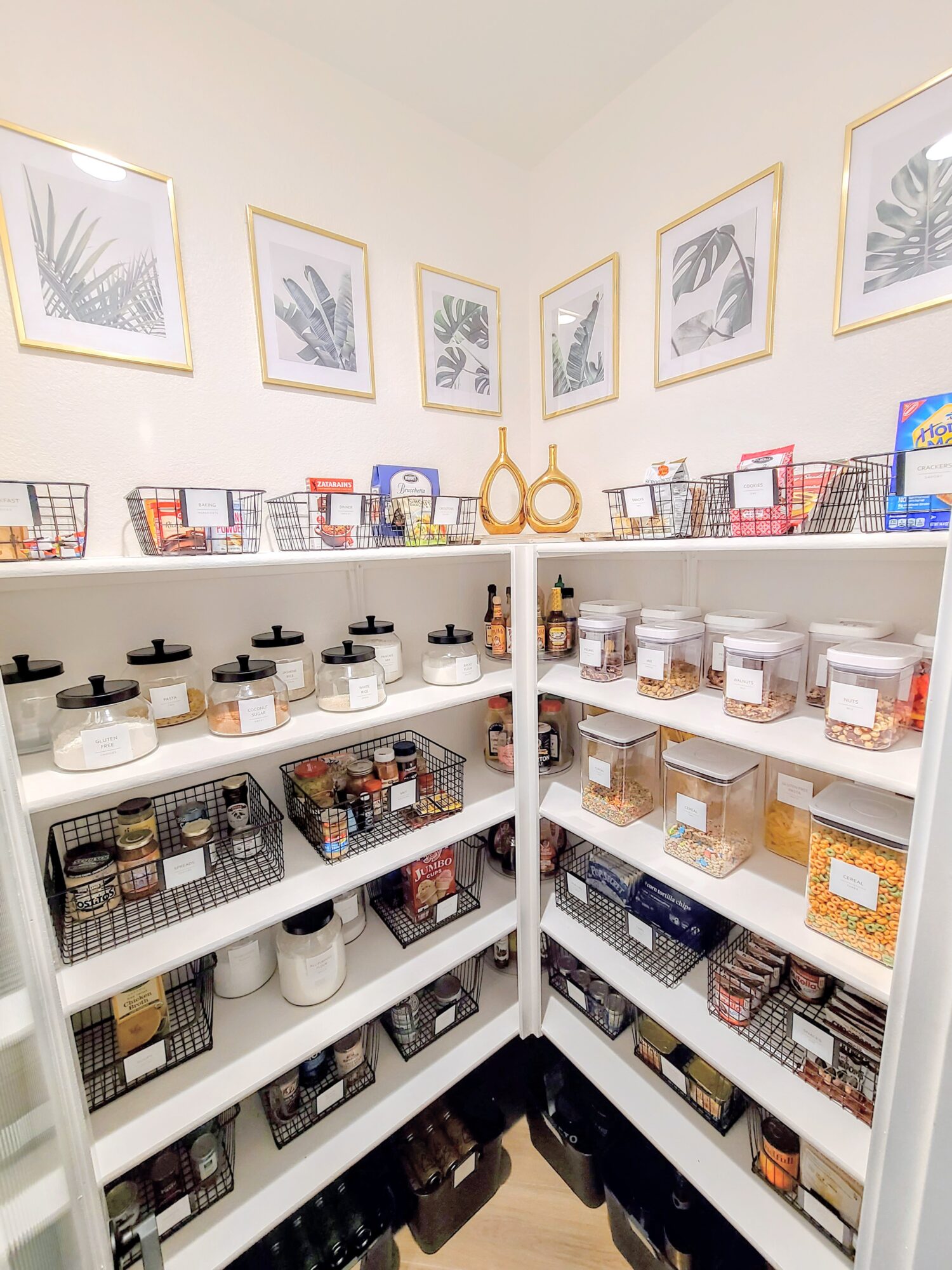 Shelves filled with jars, boxes, and baskets in a room with framed botanical prints on the wall.
