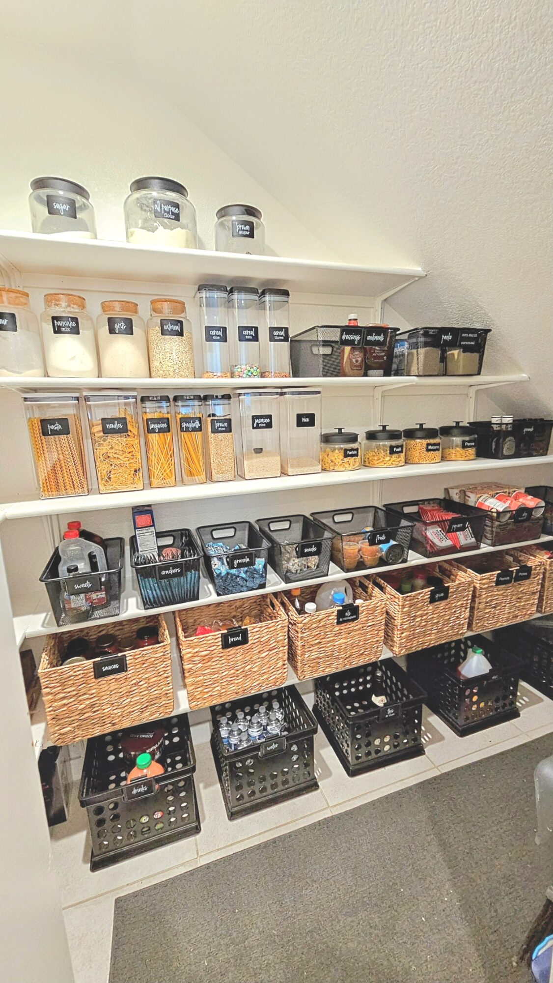 Shelves with jars, bottles, and baskets containing various food items and containers, organized neatly on a wall-mounted shelf.