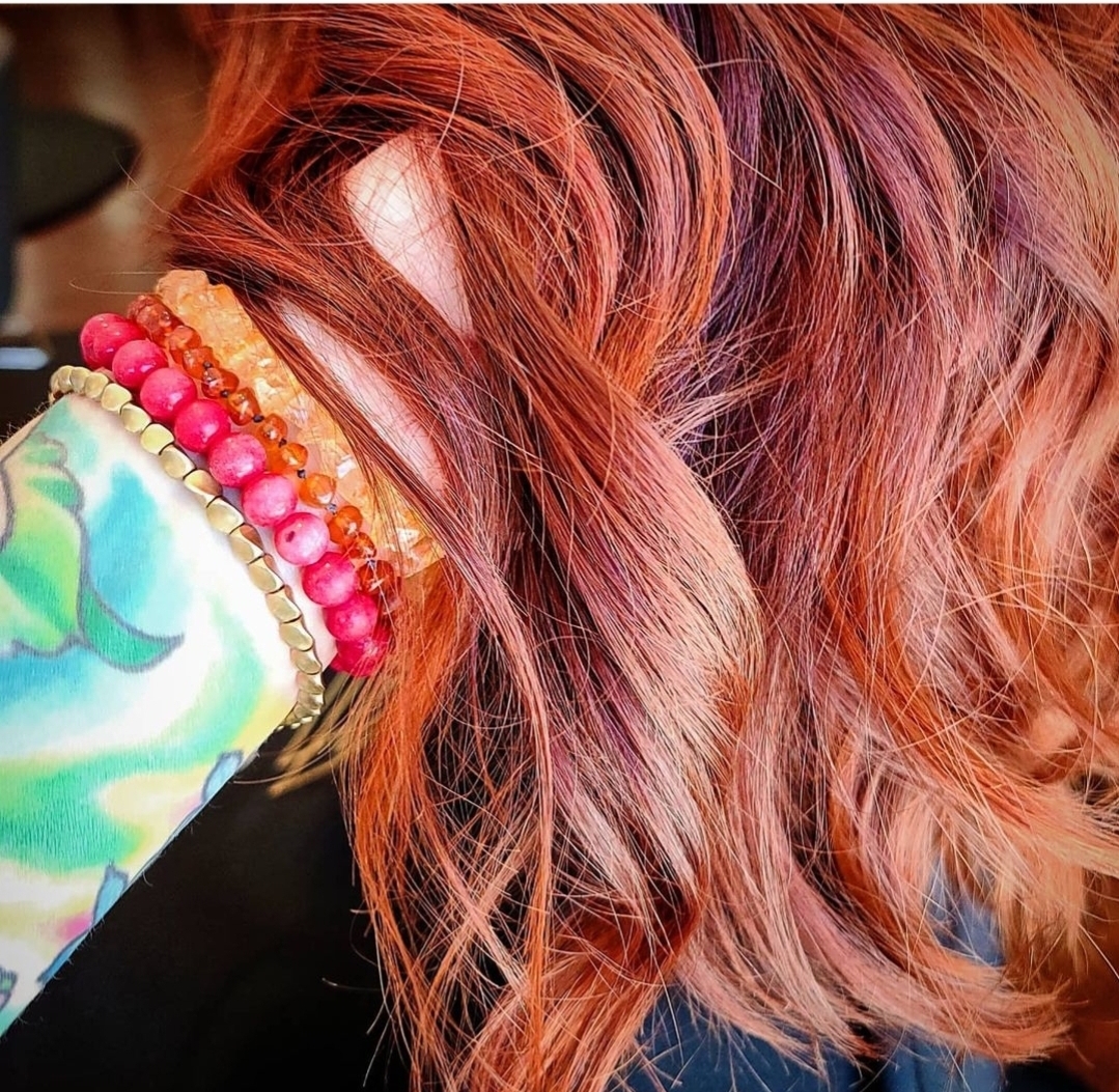 Close-up of a person's head with red hair, wearing colorful bracelets and a patterned sleeve.