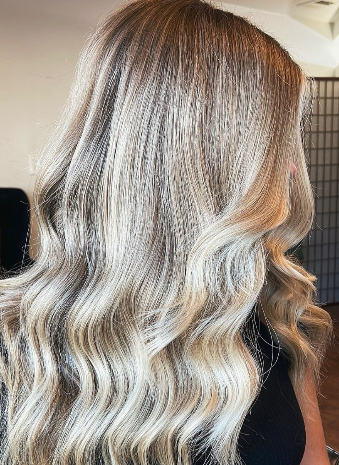 Side view of long, wavy, blonde hair with darker roots, styled in loose waves.