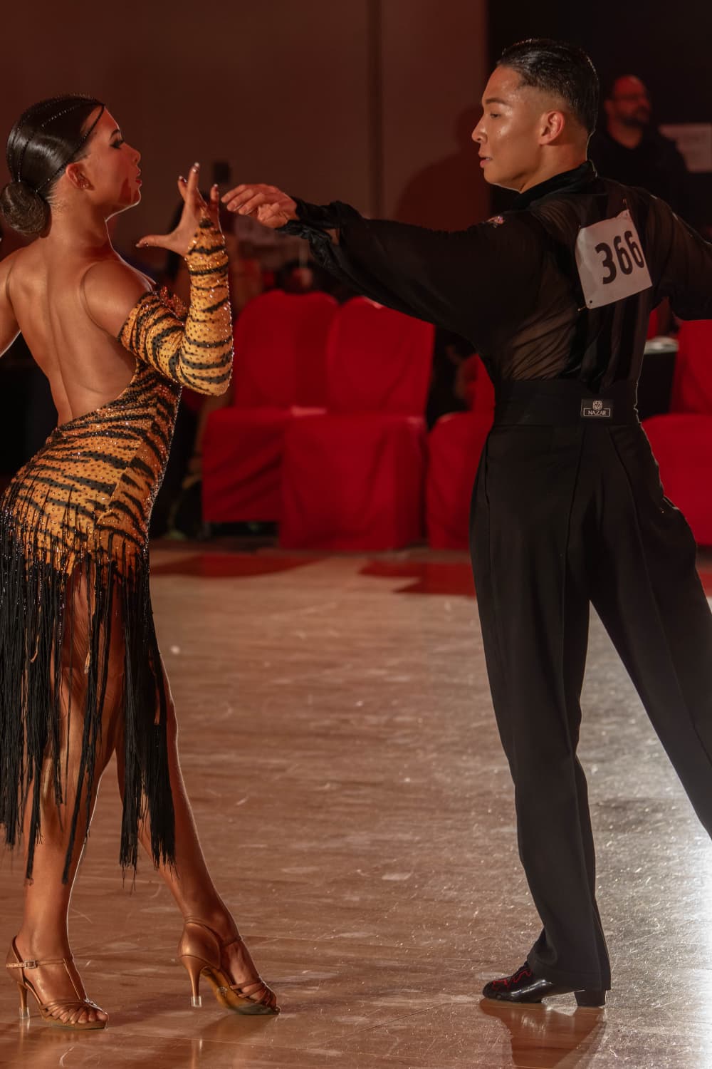 A couple dancing in a ballroom, the woman in a tiger-striped dress and the man in a black suit with a number tag.