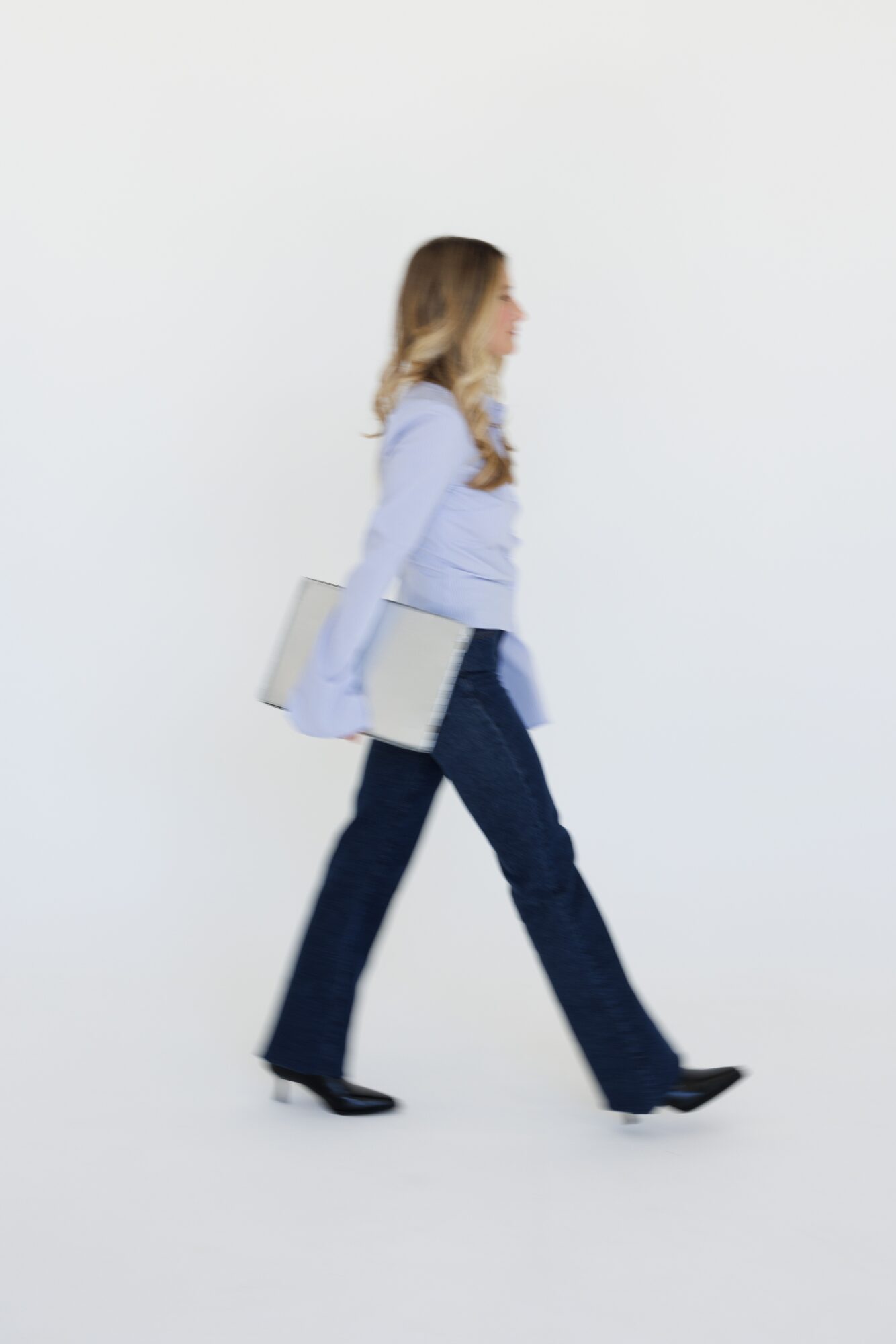 Woman walking with a laptop in her hand, side view, against a plain white background.