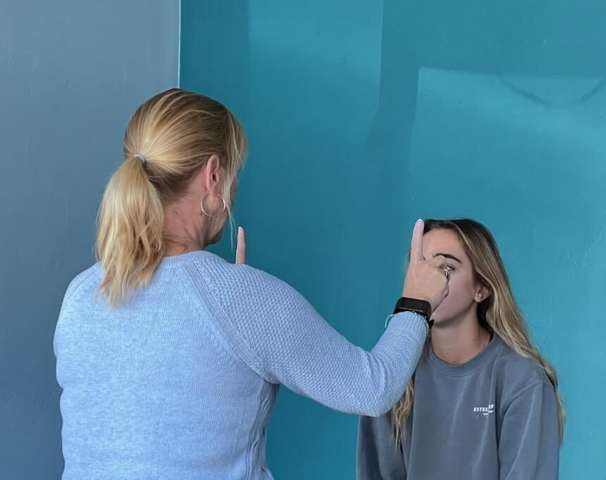 Person with blonde hair applying makeup or face paint to a young woman with long hair against a blue wall.