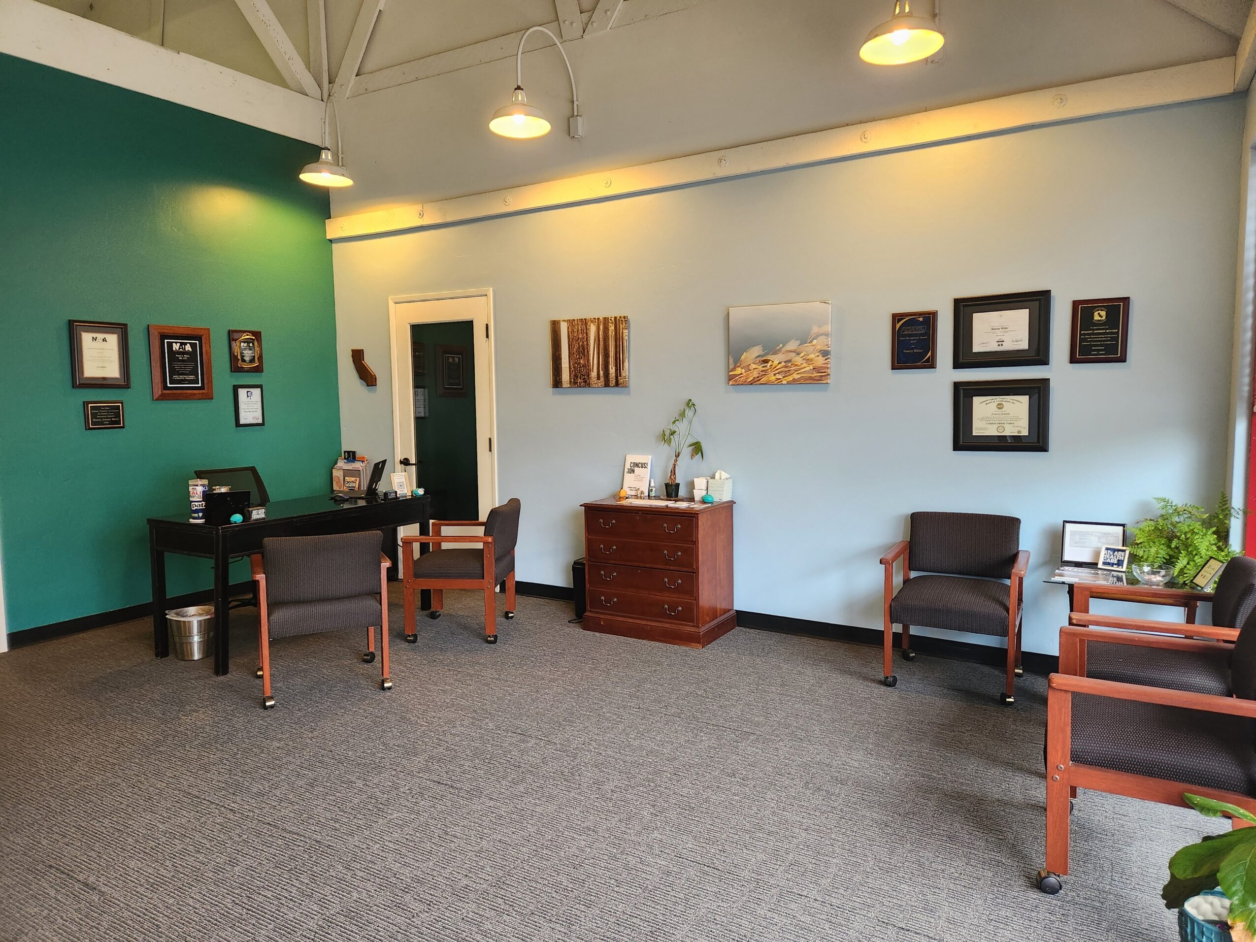 Interior of a room with green and white walls, furniture including chairs and a desk, and framed artwork on the walls.