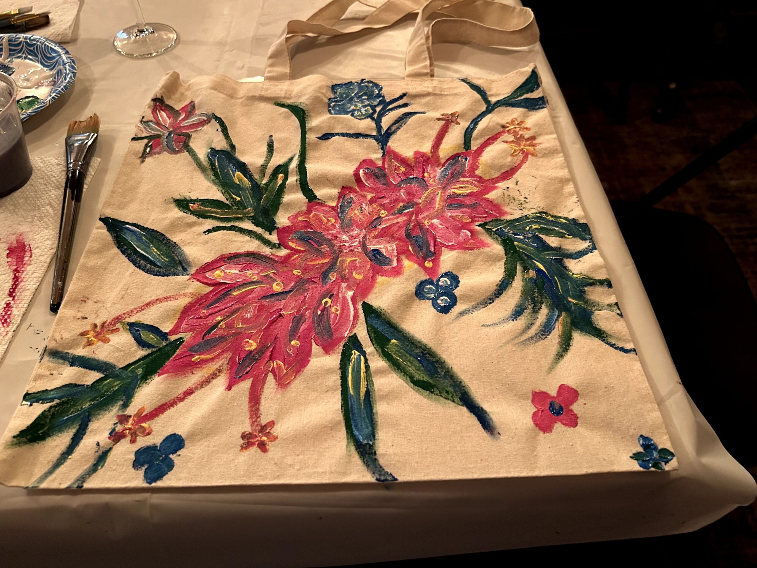 Colorful floral embroidery on fabric with pink, blue, and green threads, on a beige background, with some objects around.
