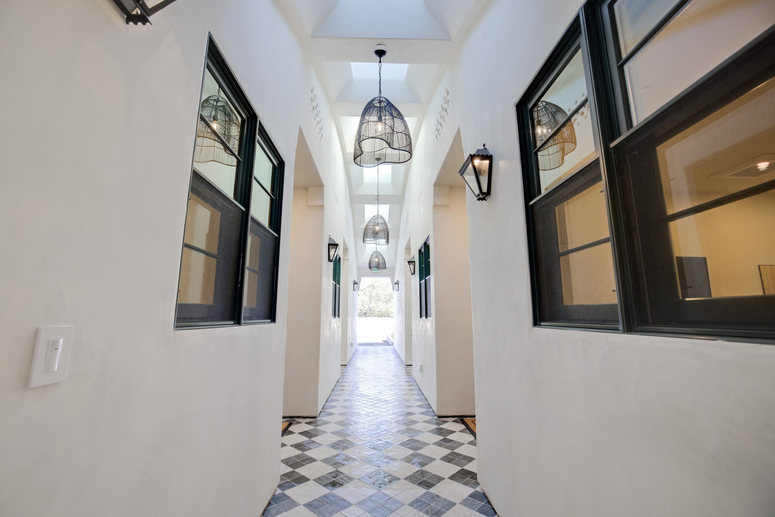 Long corridor with black-framed windows, hanging lights, and a patterned floor, leading to a bright exit.