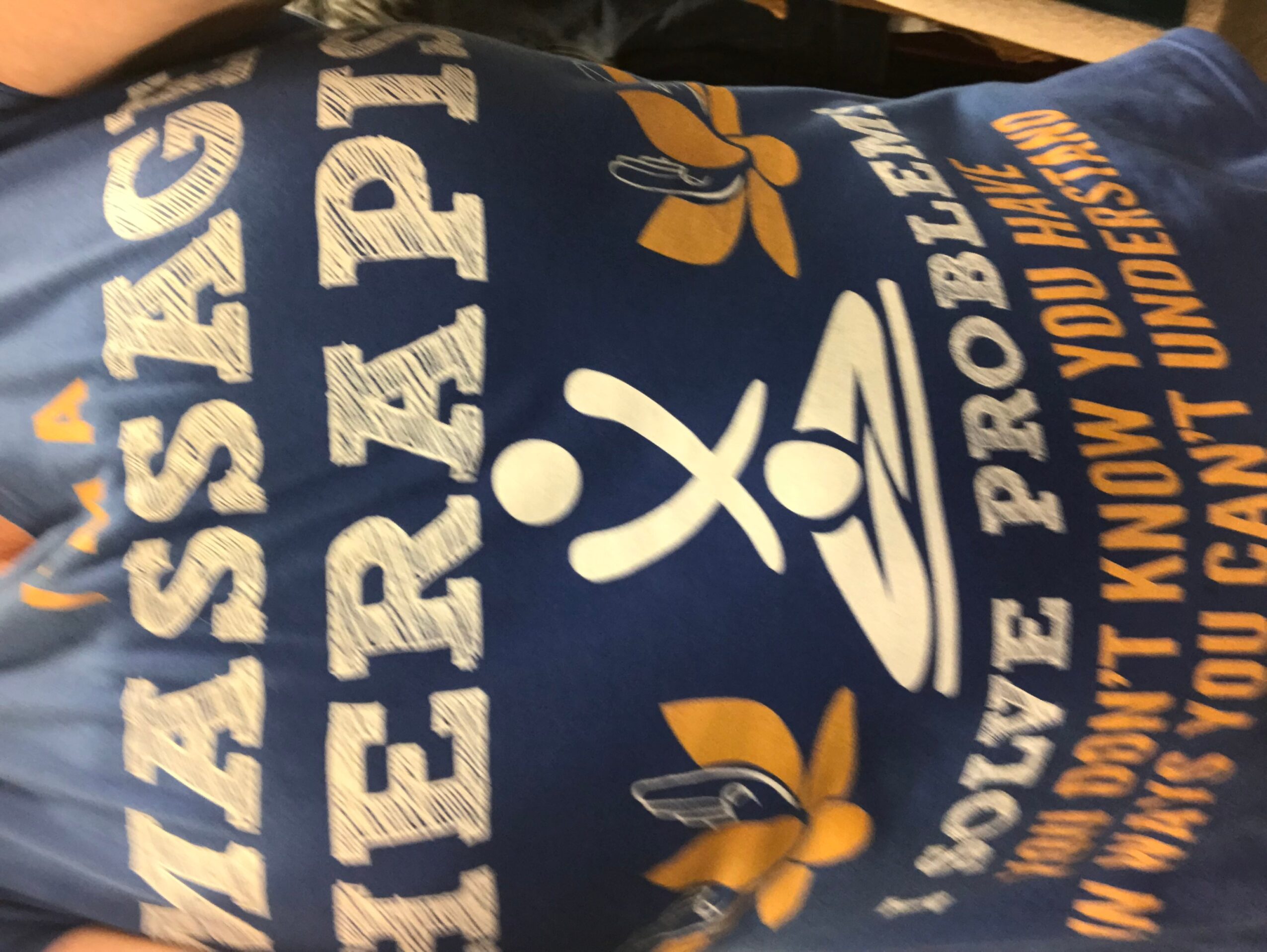 Person wearing a blue shirt with white and yellow text and graphics, lying down or leaning.