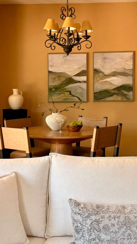 Dining room with paintings, chandelier, table, and chairs, beige wall, and a white sofa in foreground.