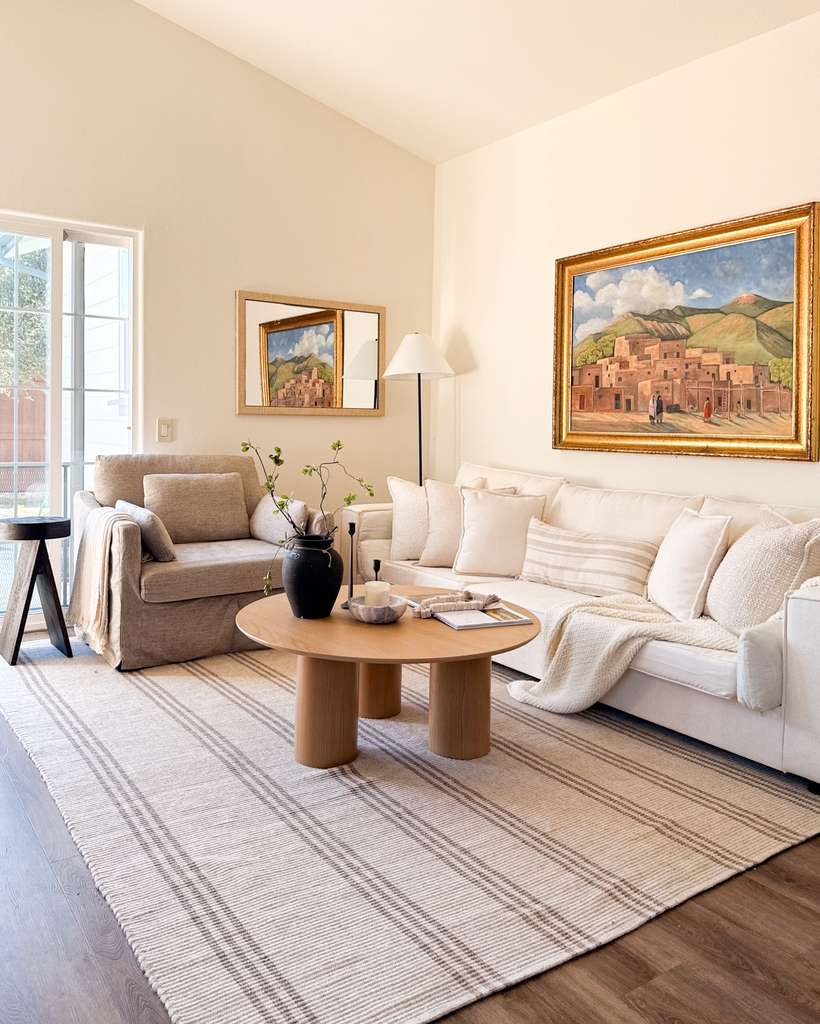 Living room with white and gray sofas, a wooden coffee table, framed paintings, a window, and a striped rug.