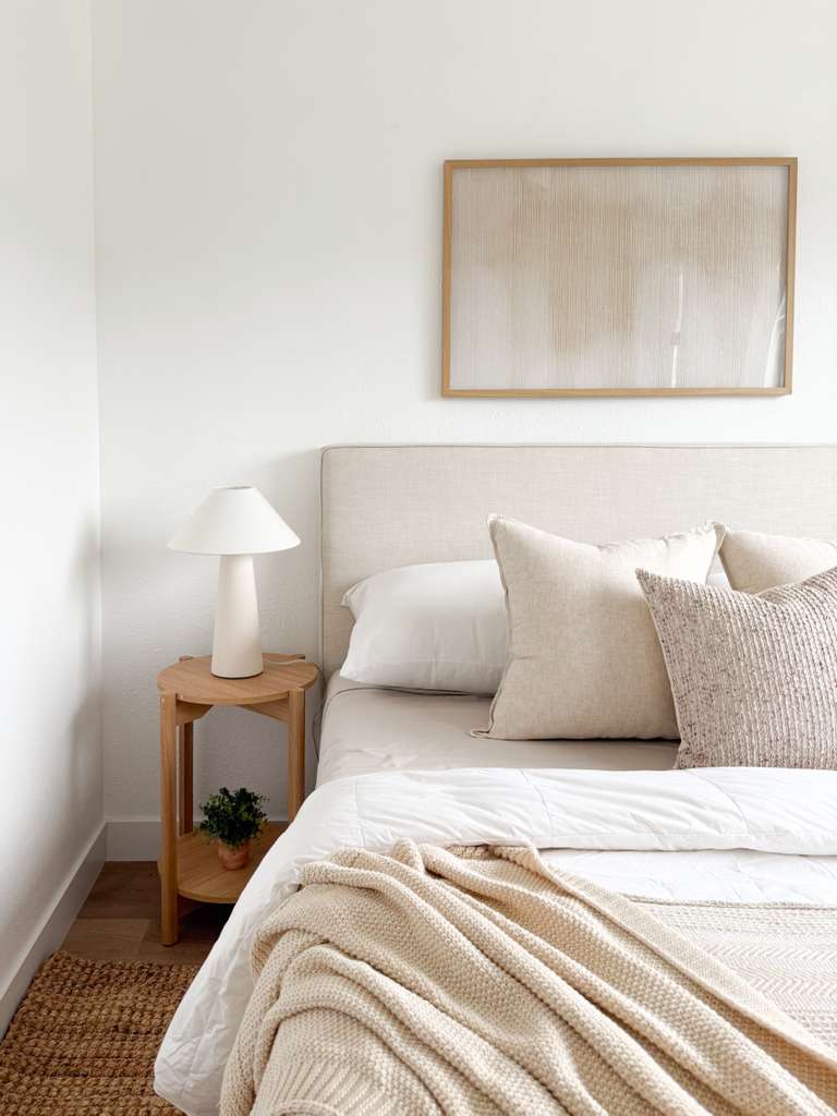 Bedroom with a bed, pillows, a nightstand with a plant, and a framed picture on the wall.