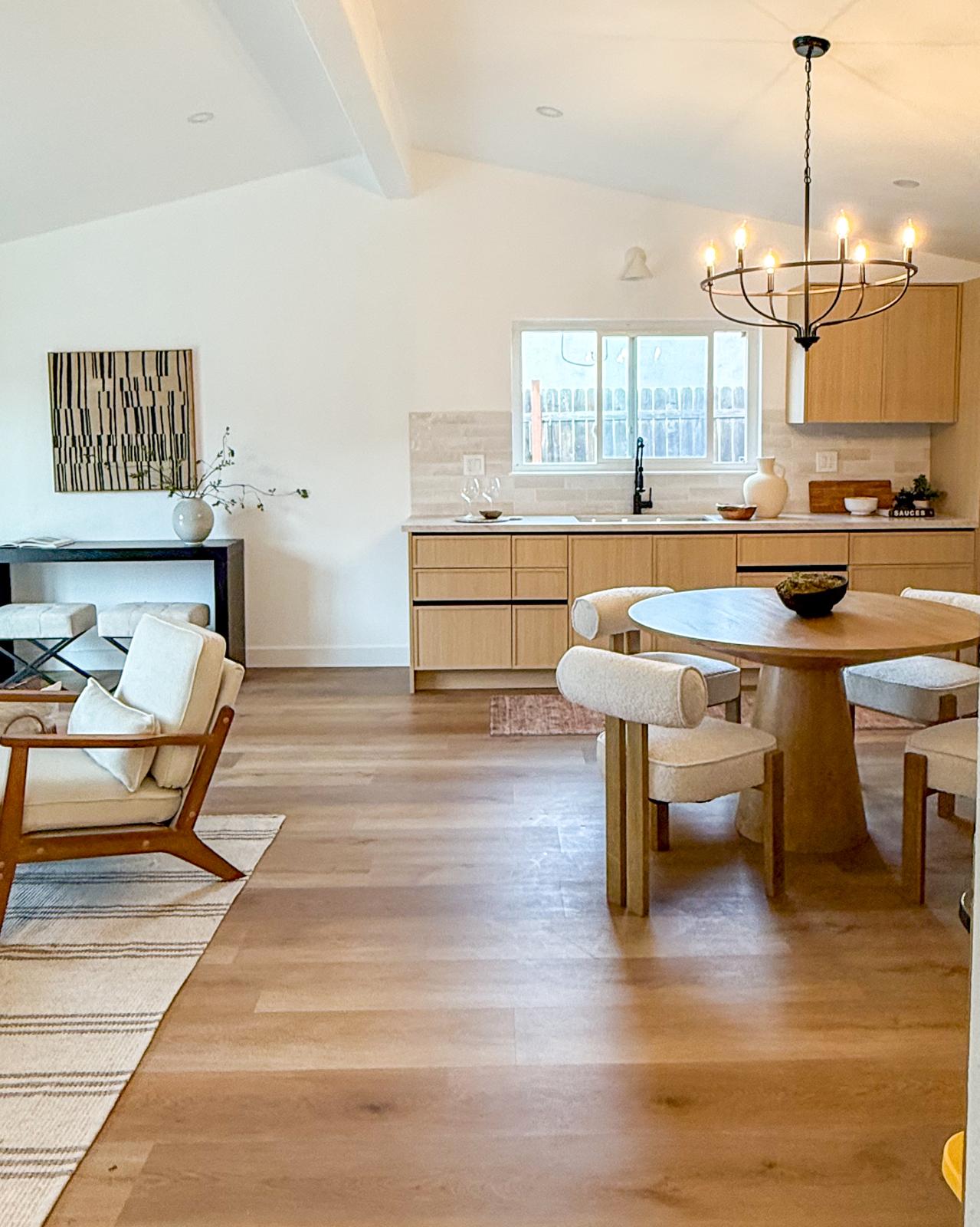 Open kitchen and dining area with wooden furniture, chandelier, and large window, bright and airy space.