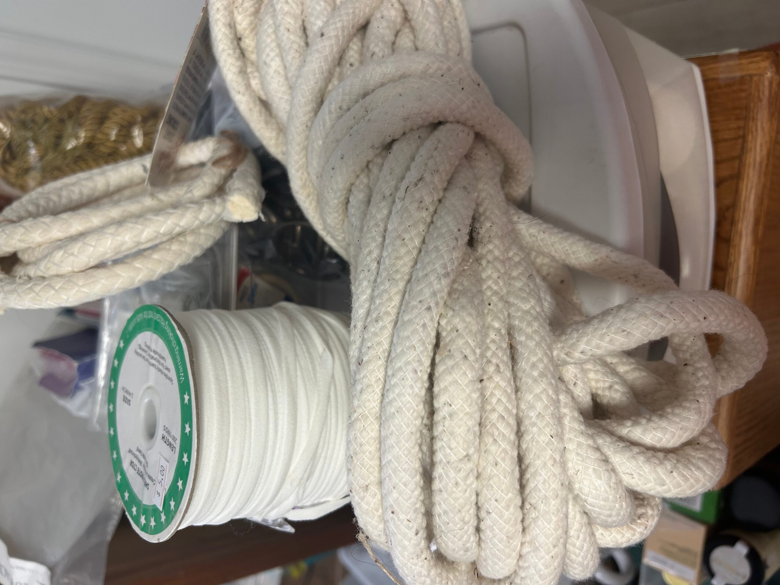 Coiled white rope with a spool of white thread nearby, on a surface with a wooden edge.