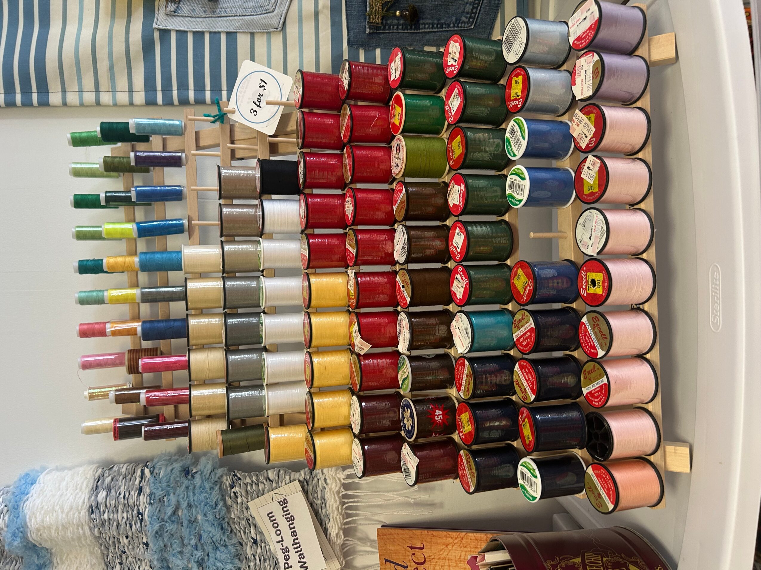 Organized collection of colorful sewing thread spools on a white circular rack.