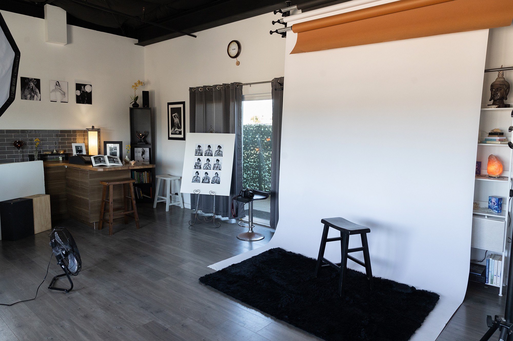 Interior of a room with a white backdrop, black stool, black rug, and shelves with decorative items.