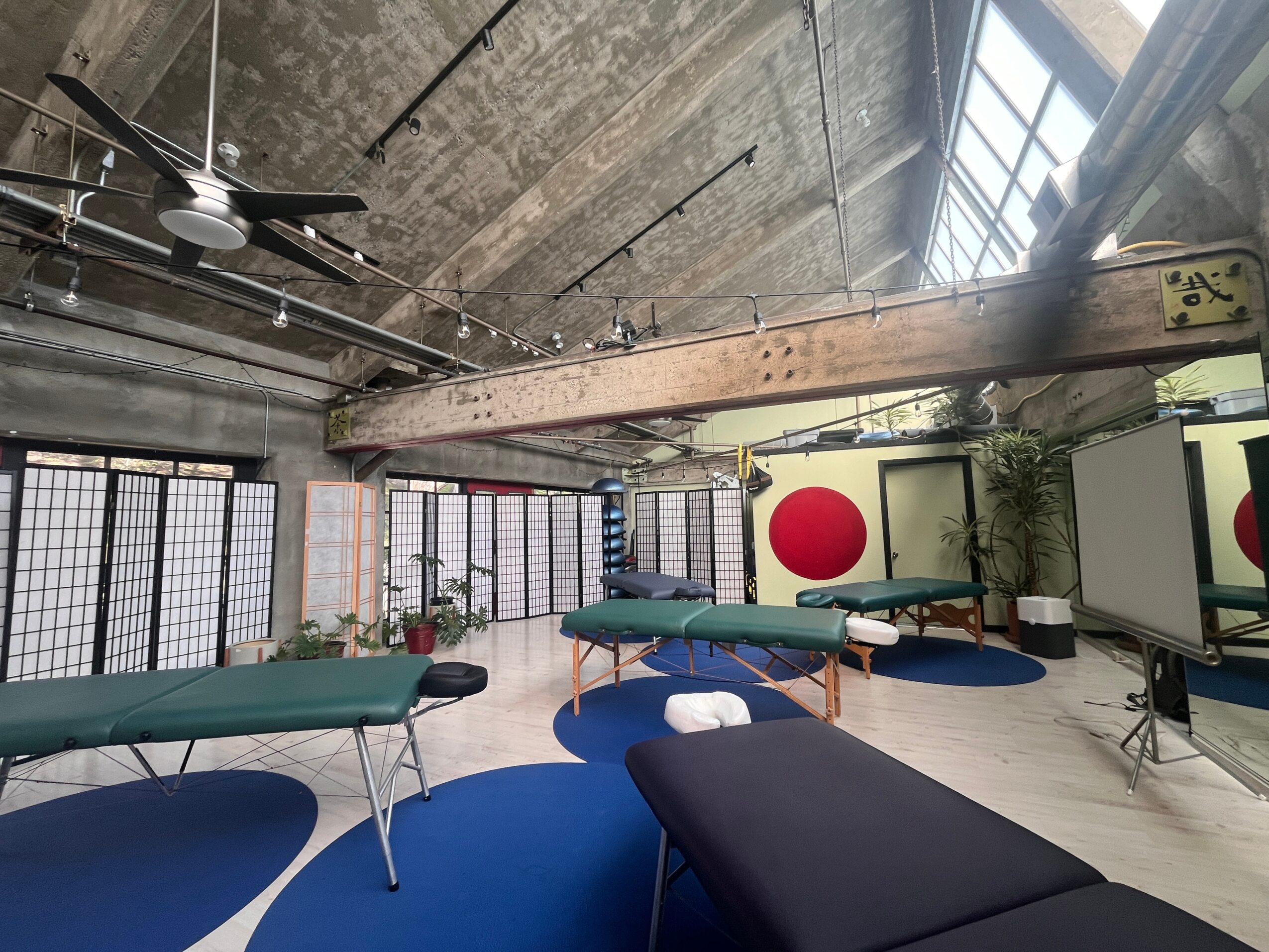 Indoor space with massage tables, large windows, and a Japanese flag, illuminated by natural light.