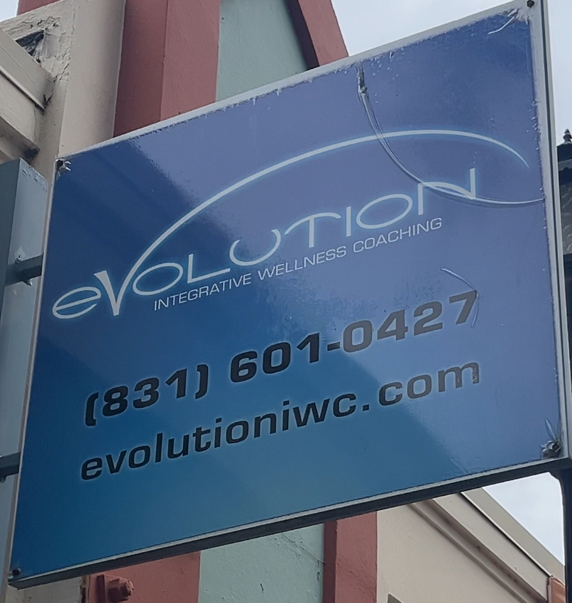 Blue sign with white text advertising Evolution Wellness Coaching, including phone number and website.