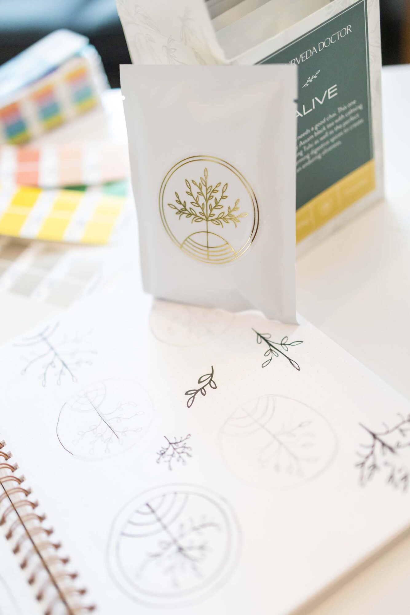 White paper bag with gold tree logo, surrounded by sketches and color swatches, on a white surface.