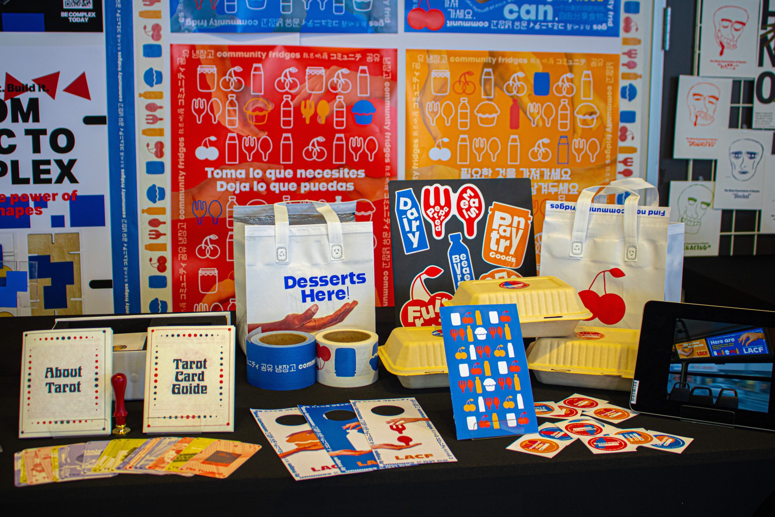 Display of colorful cards, bags, and small items on a table with packaging and signs in the background.