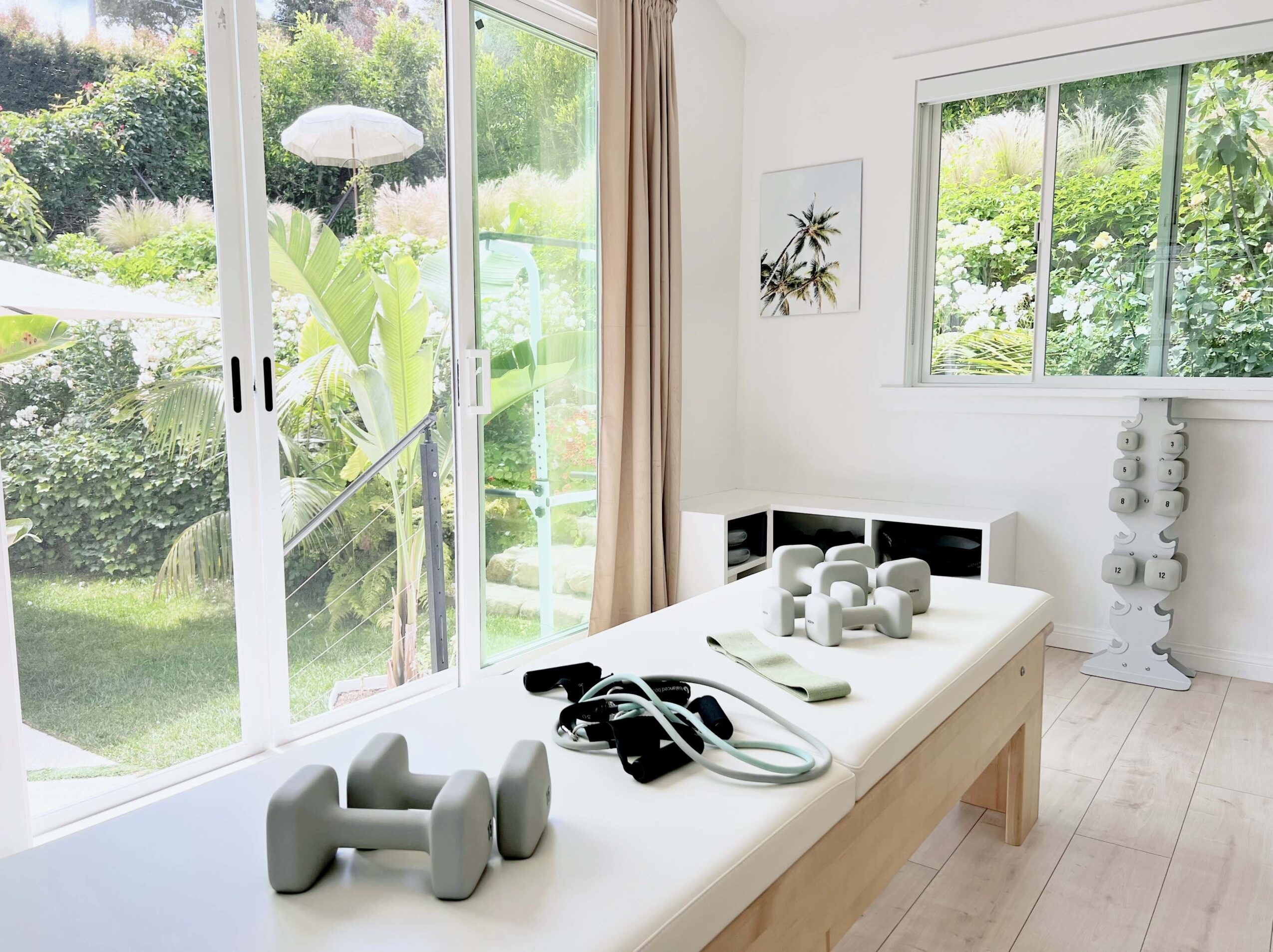 Bright room with large windows showing greenery outside, a table with white objects, and a small black and white cabinet.