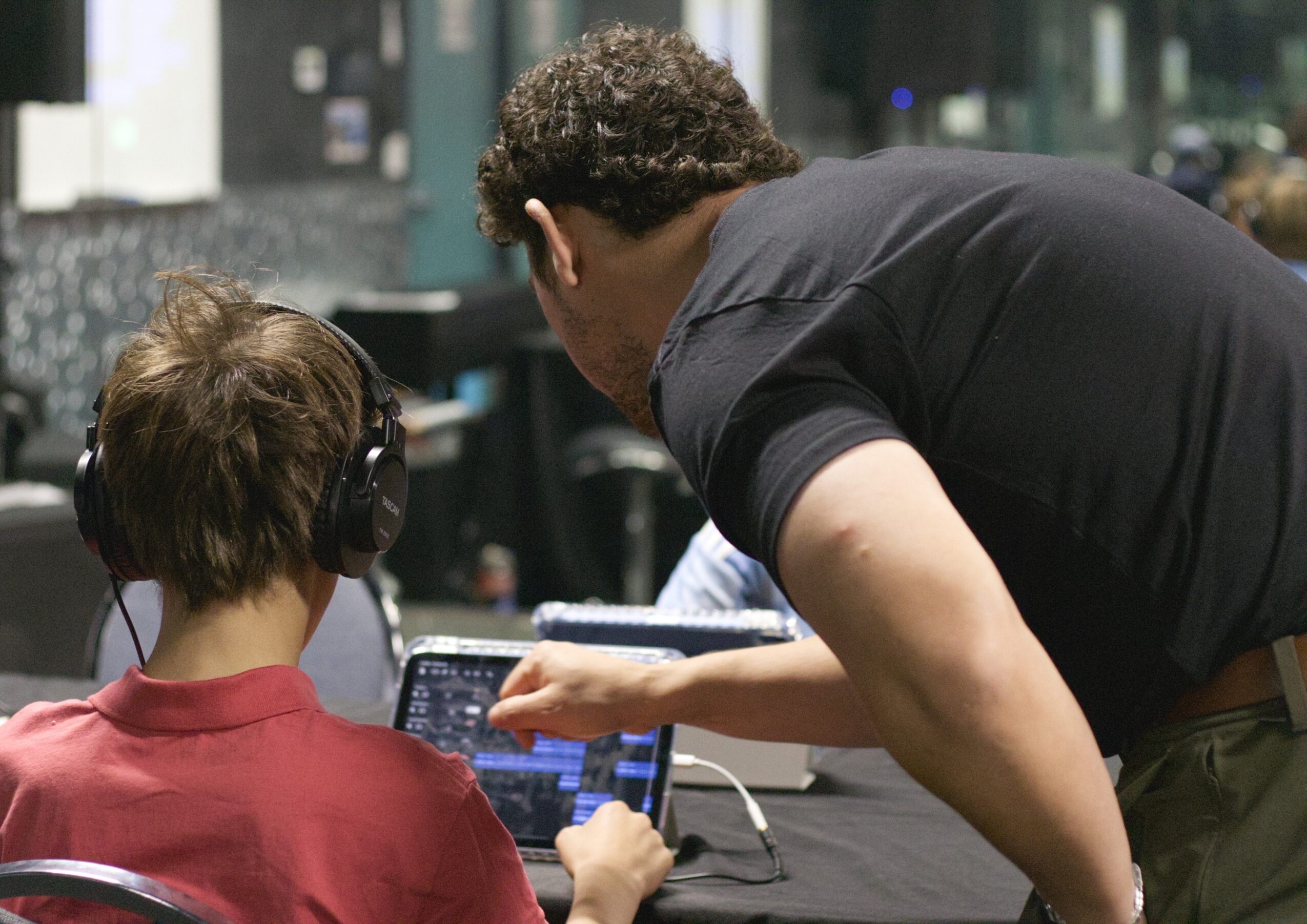 Two people in a recording studio, one with headphones, the other pointing at a tablet screen.
