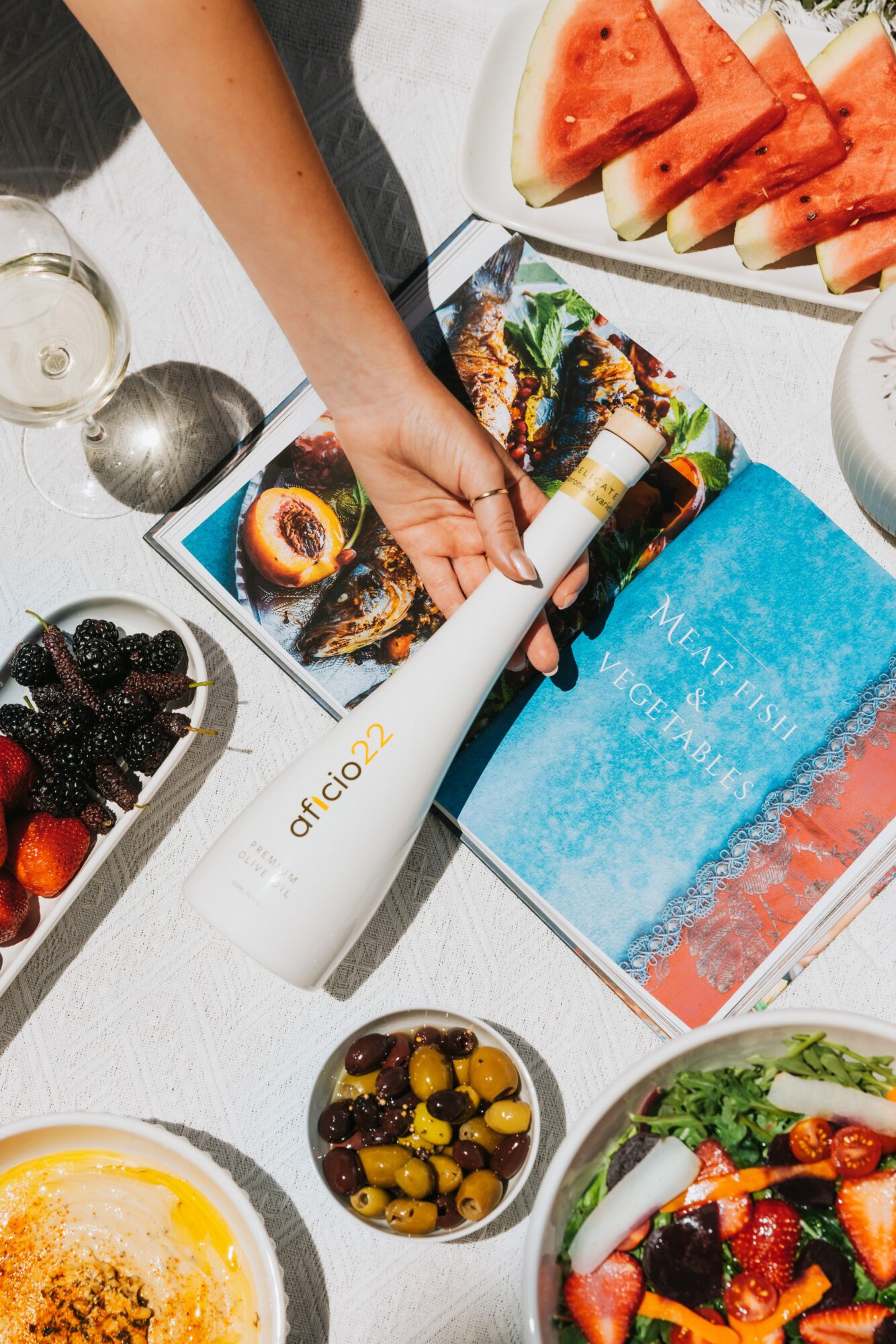 Person slicing watermelon on a white table with various fruits and a colorful magazine, with a white device labeled 'afinoz'.
