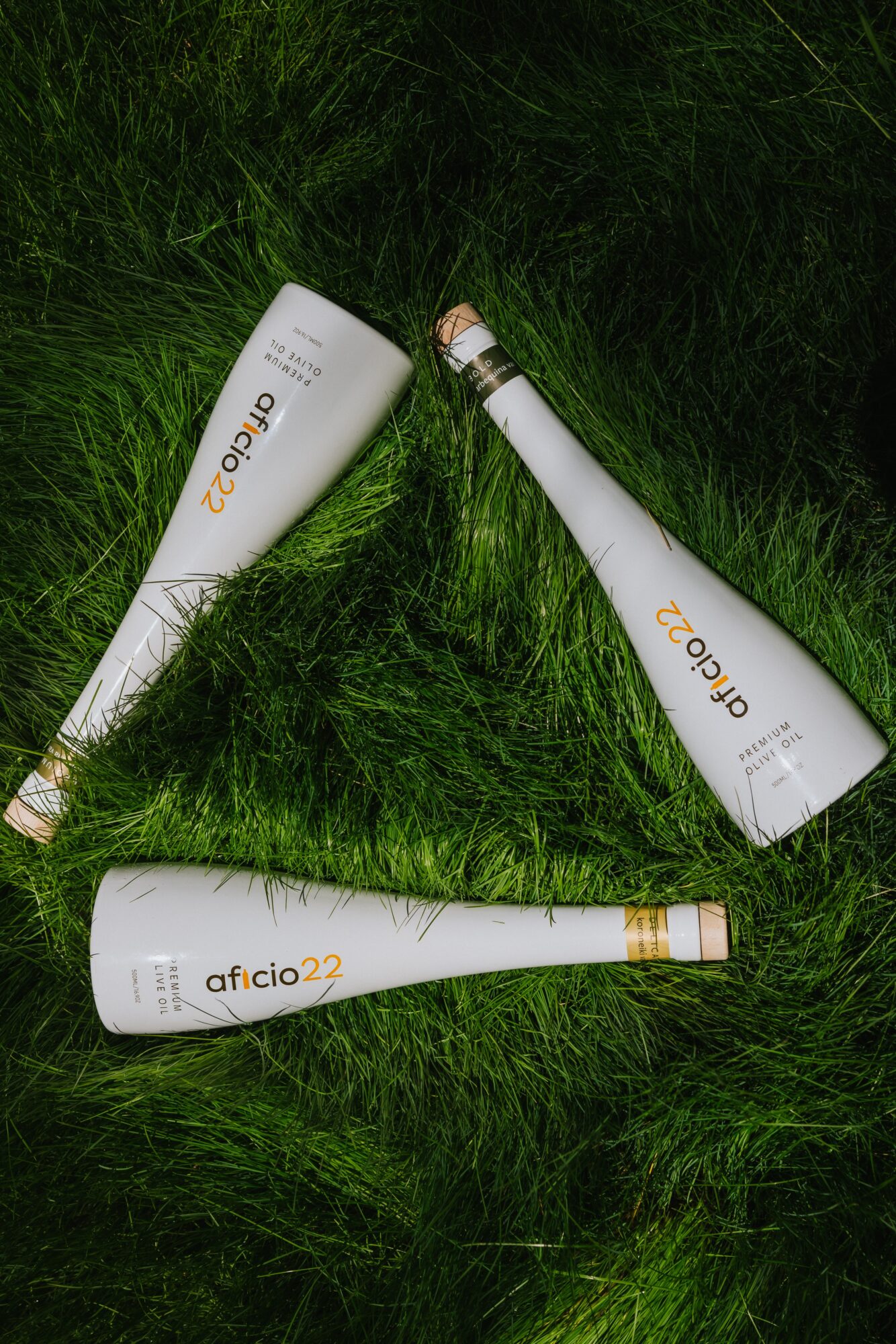 Three white bottles with gold caps and labels on green grass, arranged in a triangle.