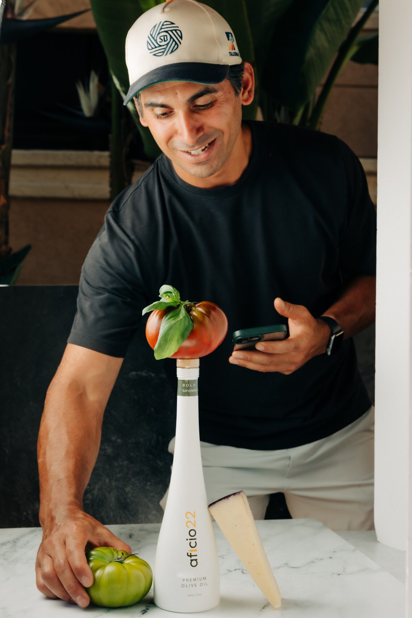 Man wearing a helmet, smiling, holding a smartphone, with a green apple and a white vase on a table.