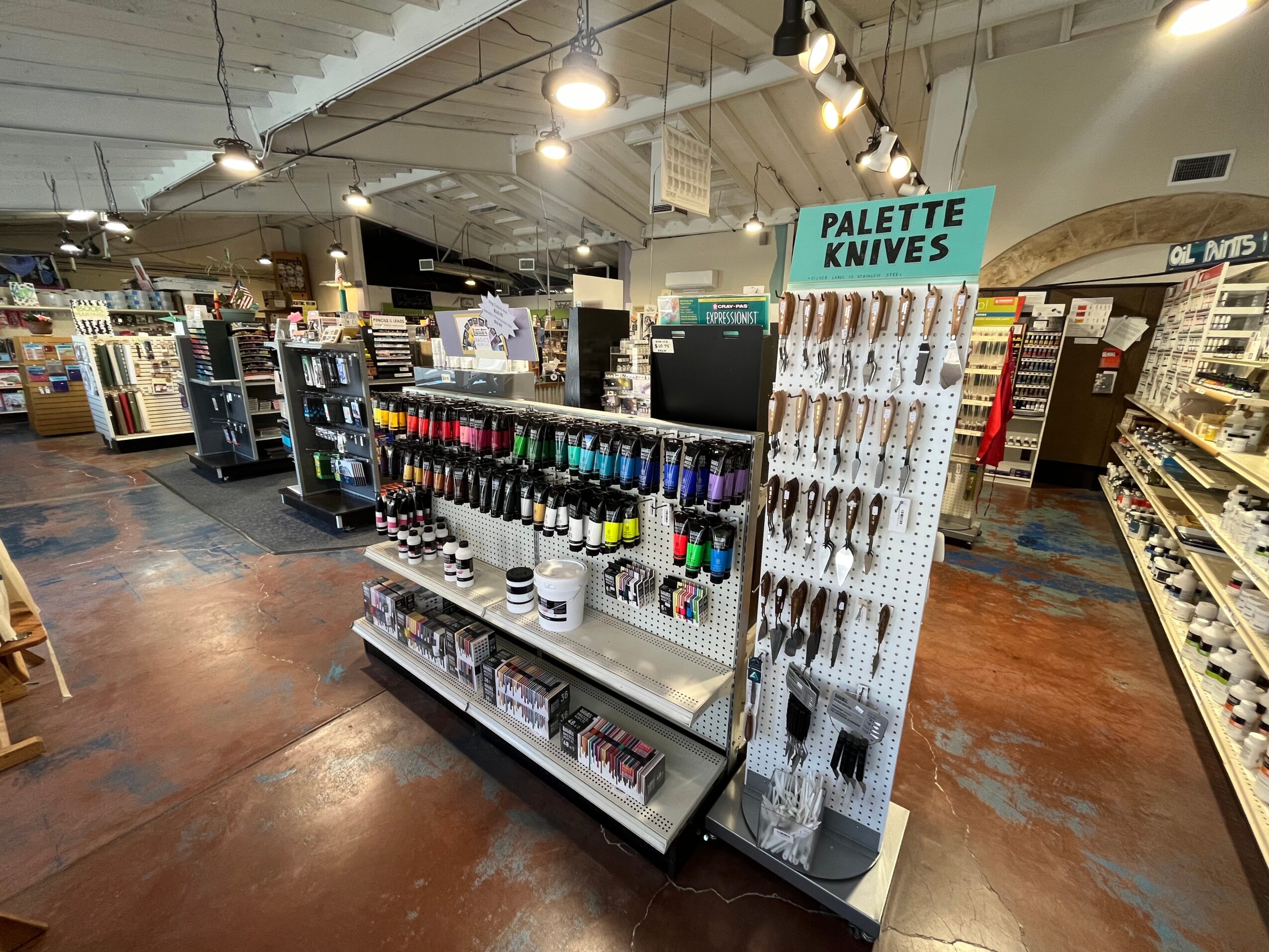 A store aisle with shelves of knives and kitchen tools, including a display labeled 'PALETTE KNIVES'.