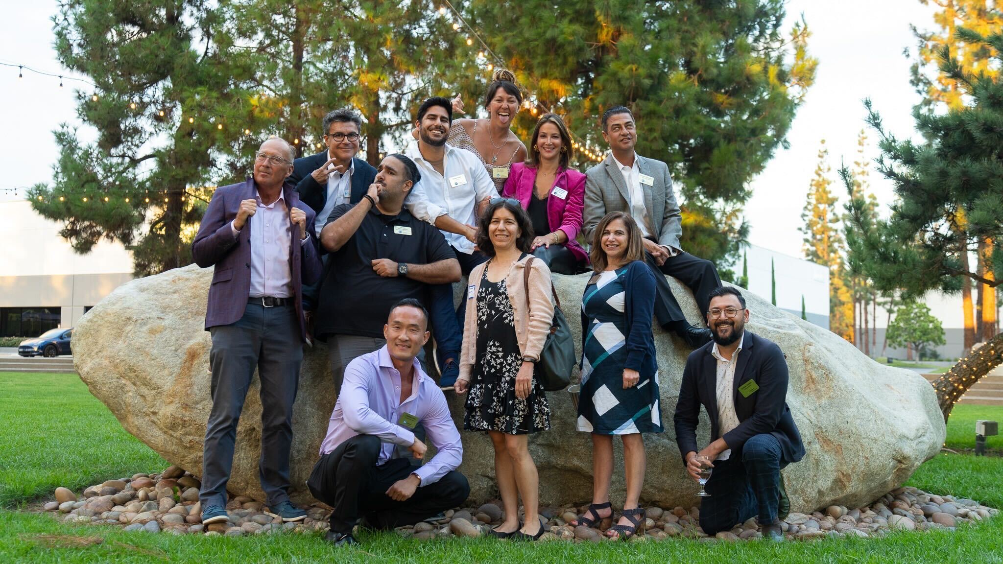 Group of ten people outdoors in front of trees and a large rock, smiling and posing for a photo.