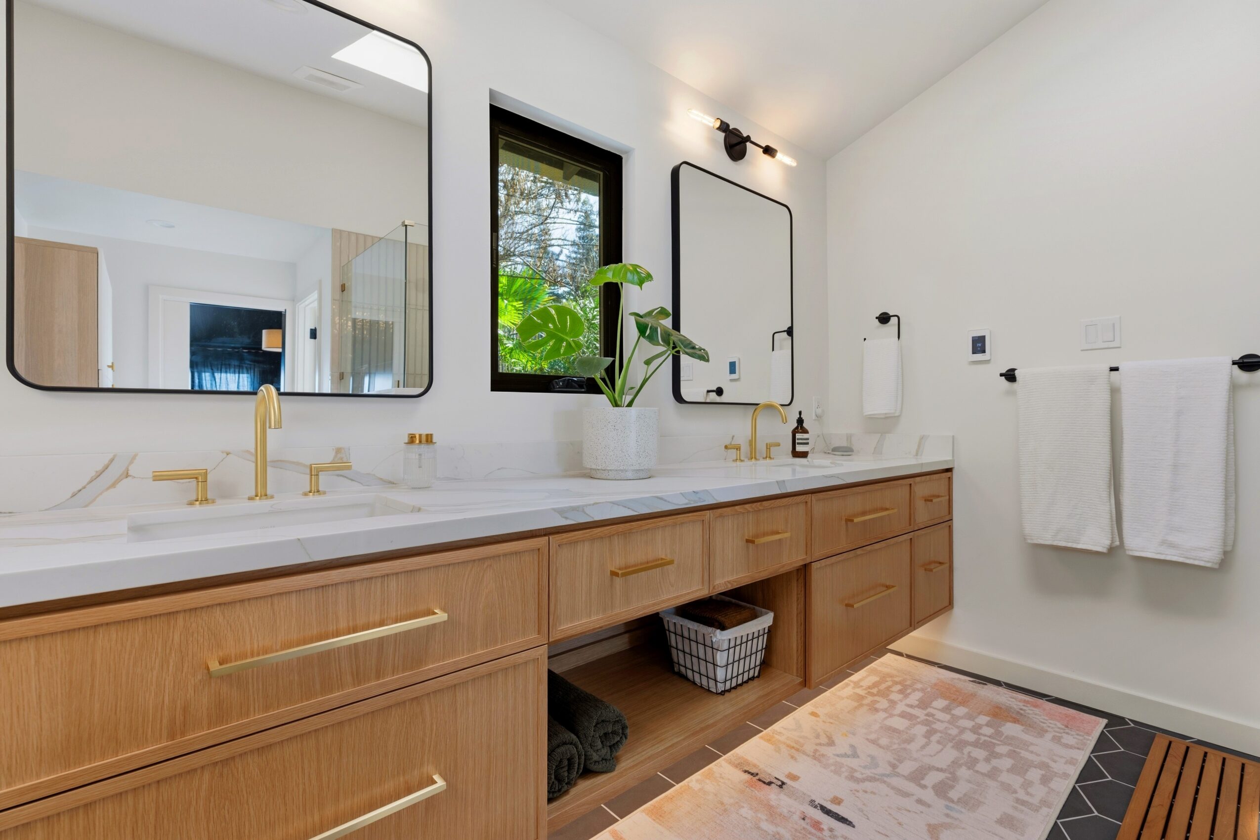 Bathroom with double sink vanity, large mirror, window, and towels on wall, with a rug on the floor.