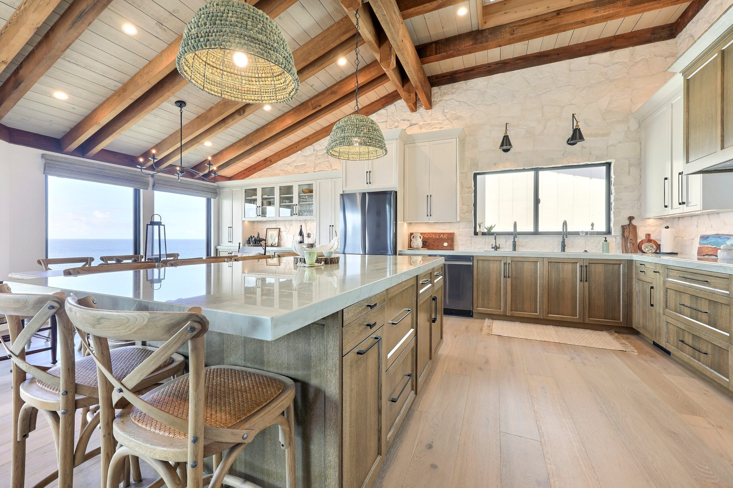 Bright kitchen with wooden ceiling beams, large island, and windows showing a view outside.
