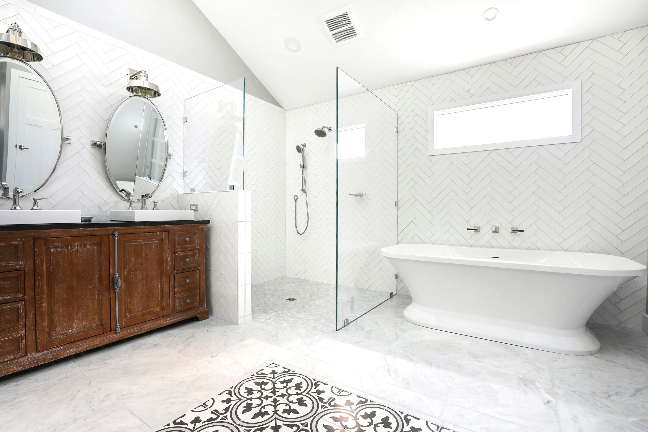 Bathroom with double vanity, walk-in shower, and bathtub, featuring white walls, a window, and patterned floor tiles.
