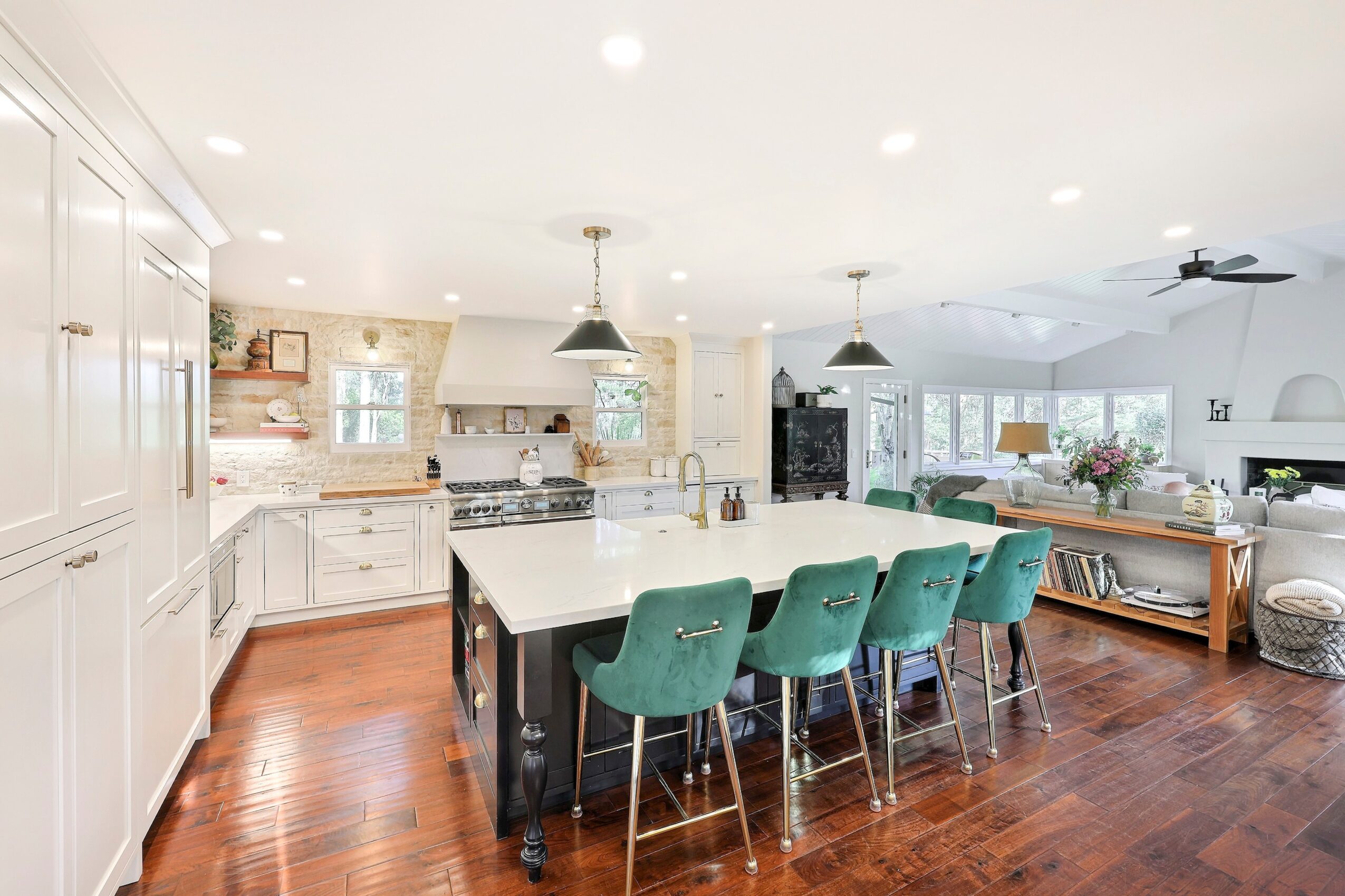 Open-concept kitchen and living area with white cabinets, a large island with teal chairs, hardwood floors, and modern decor.