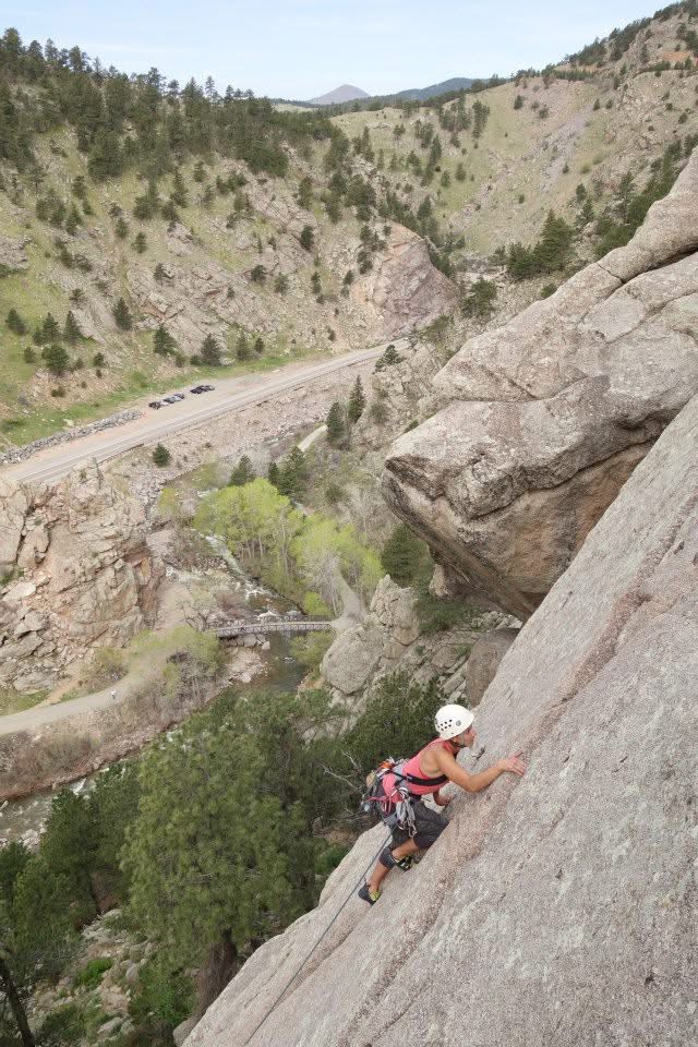Person wearing a helmet and climbing gear ascending a steep rock face in a mountainous landscape.
