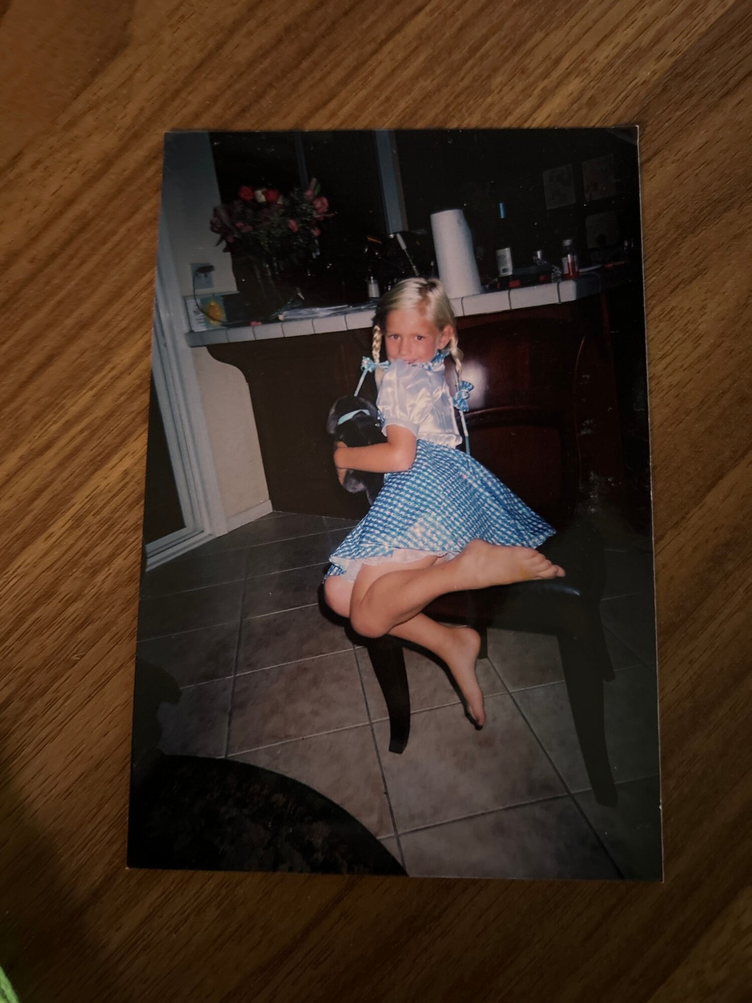 Person in a blue dress sitting on a chair with one leg crossed over the other, in an indoor setting.