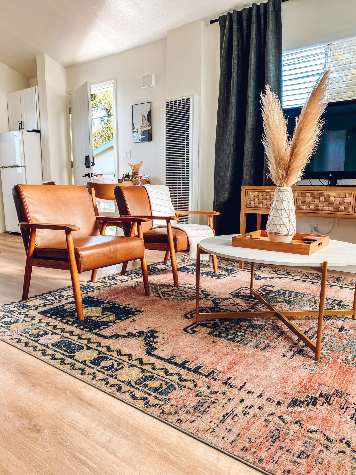 Living room with two brown leather armchairs, a white chair, a wooden coffee table with a vase of pampas grass, and a patterned rug.