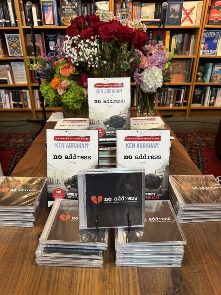 Books titled 'no address' by Ken Abrahaman displayed on a table with a large flower arrangement in the background, in a bookstore.