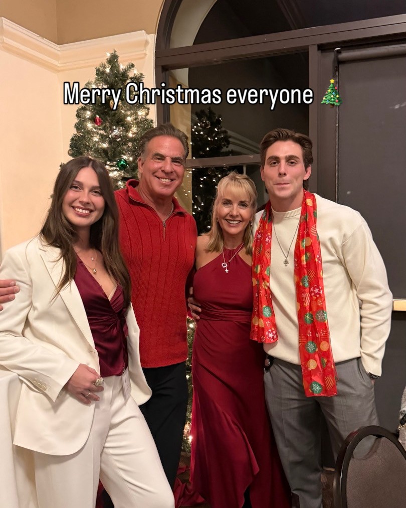 Four people standing in front of a decorated Christmas tree, smiling, with a window in the background, celebrating Christmas.