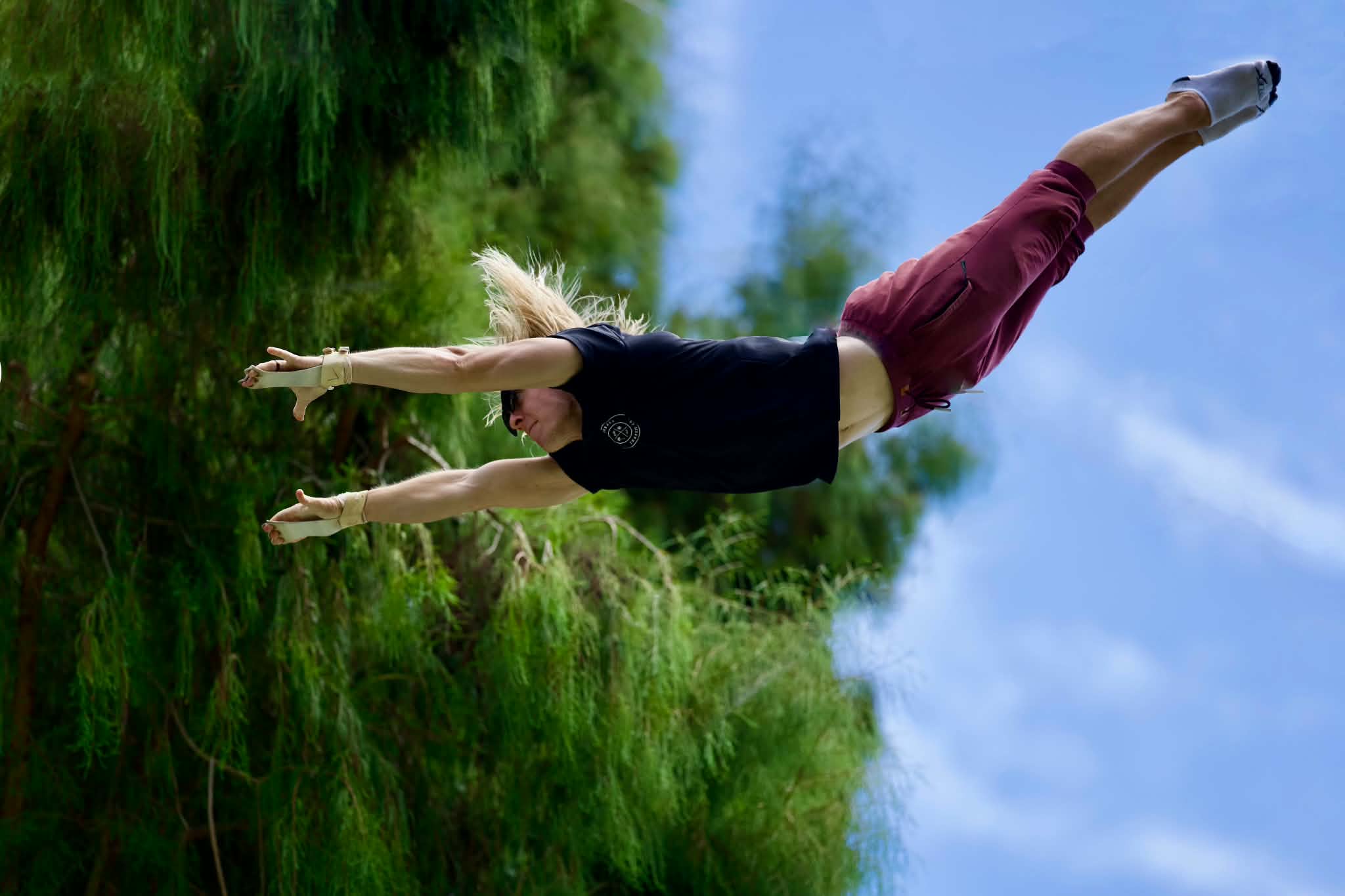 Person in mid-air outdoors with arms extended, grass and blue sky in background.
