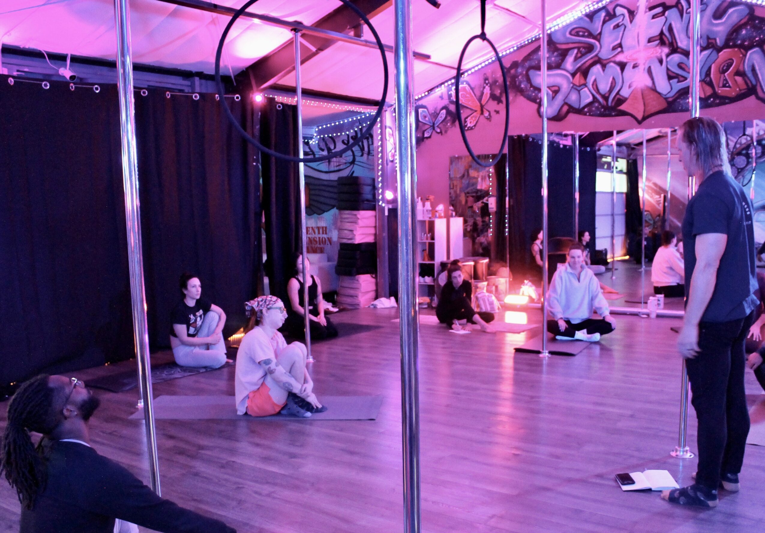 People sitting on the floor in a dance studio with mirrors and colorful graffiti on the walls.