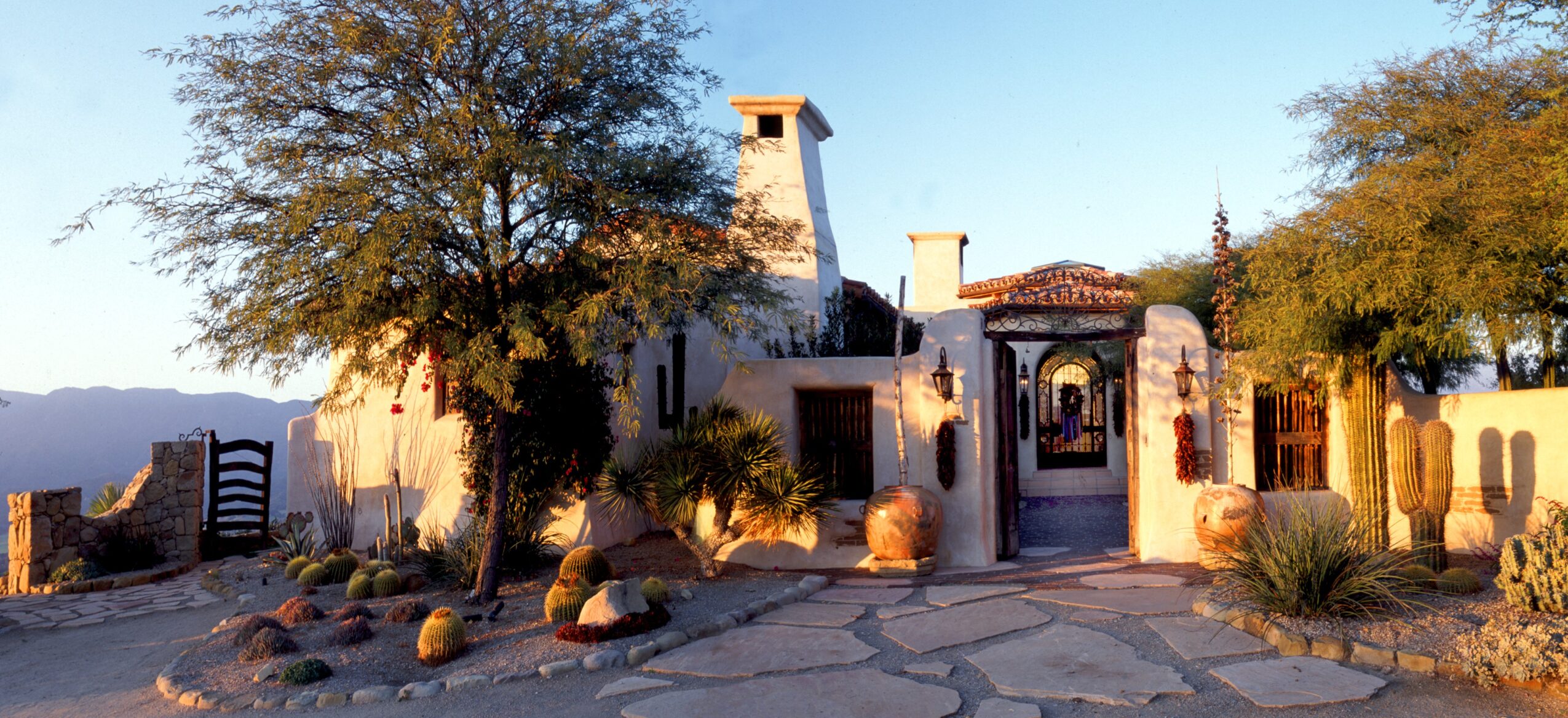 A building with a gated entrance, surrounded by trees and desert plants, under a clear blue sky.