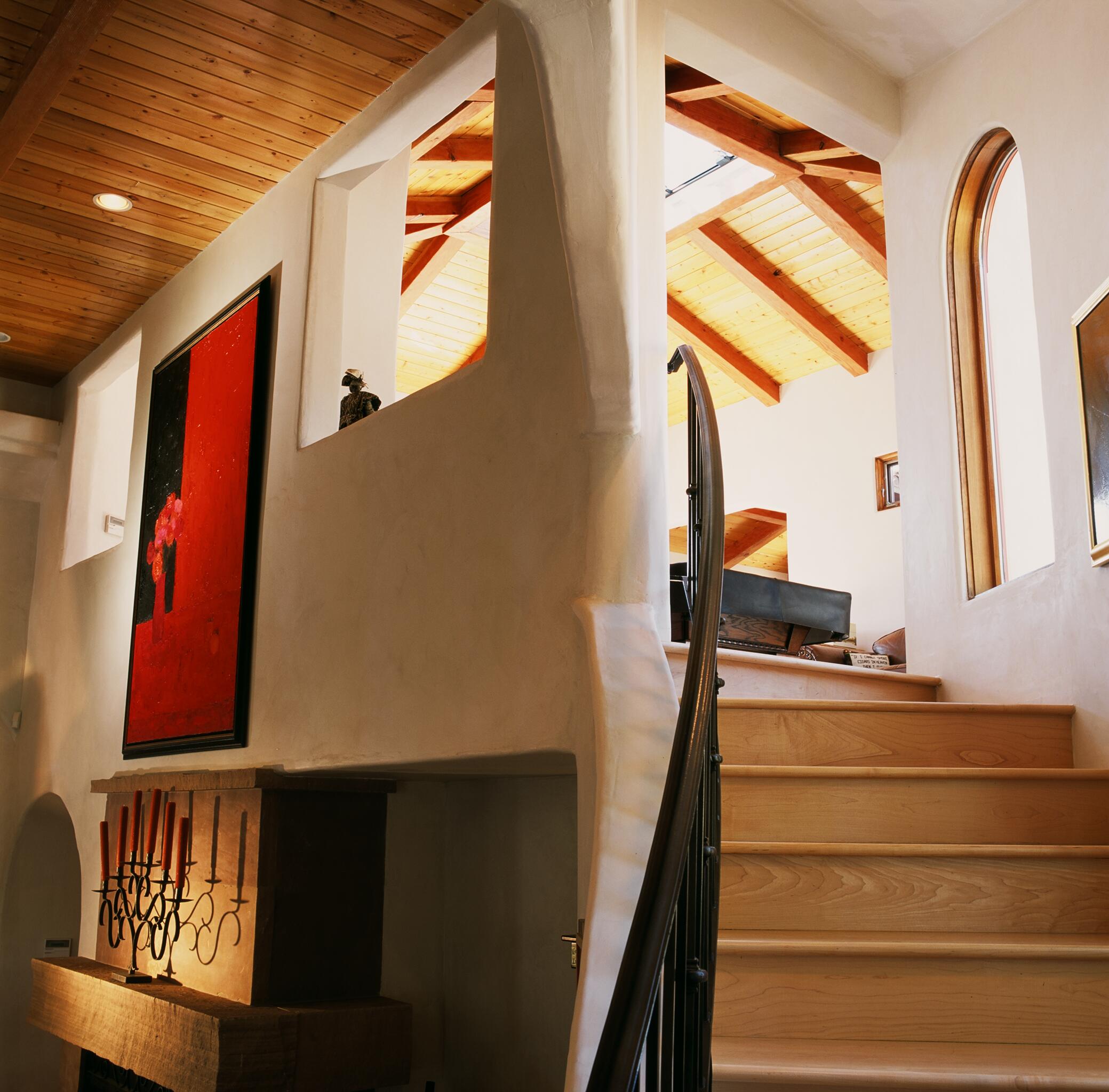 Interior view of a staircase with wooden steps, a curved white wall, and a window with an arched top, sunlight streaming in.