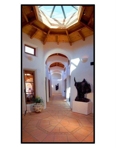 Interior hallway with arched ceiling, wooden accents, and sculptures, illuminated by natural light from skylight and windows.