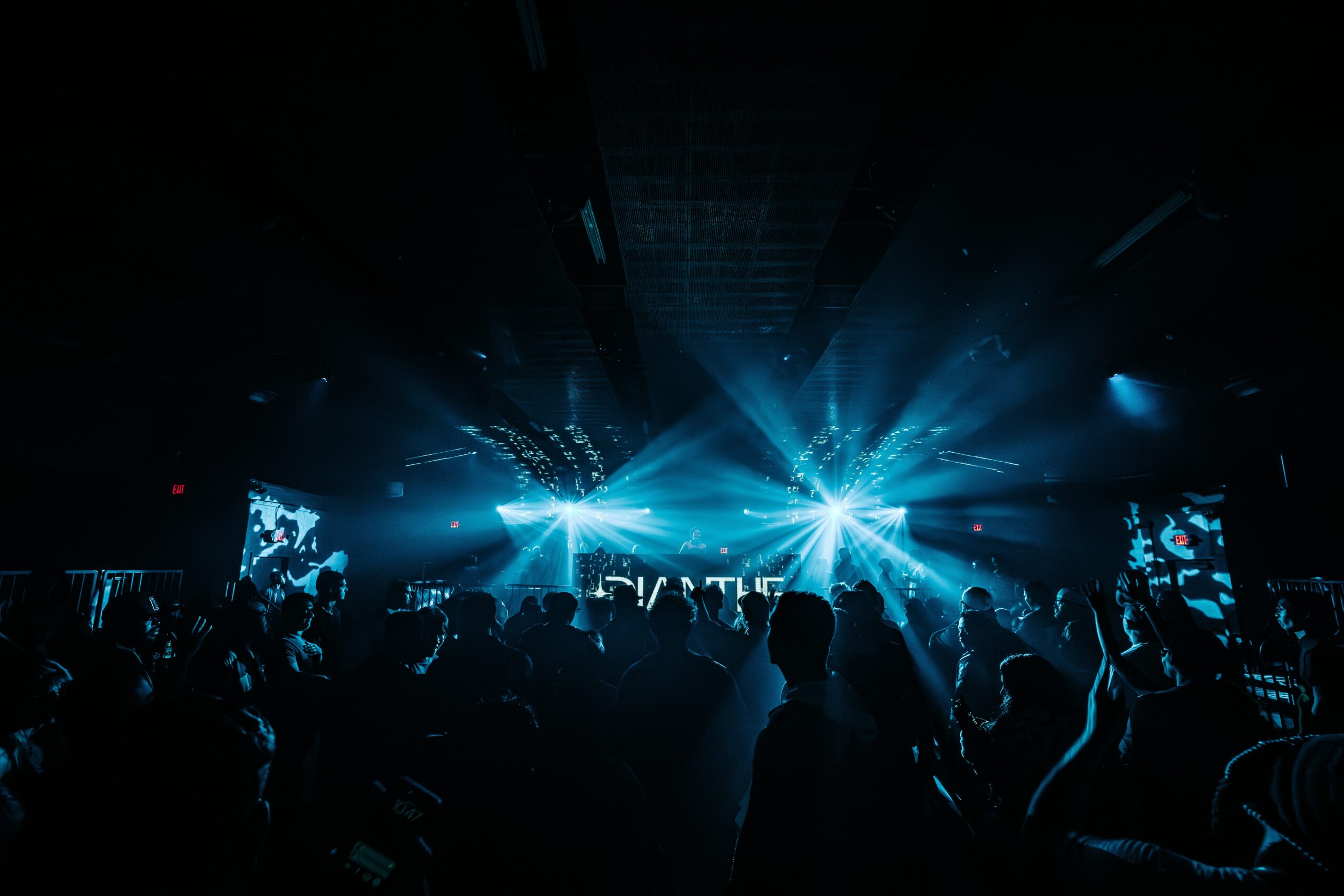 Crowd at a concert with bright blue stage lights and silhouettes of people dancing and enjoying the event.