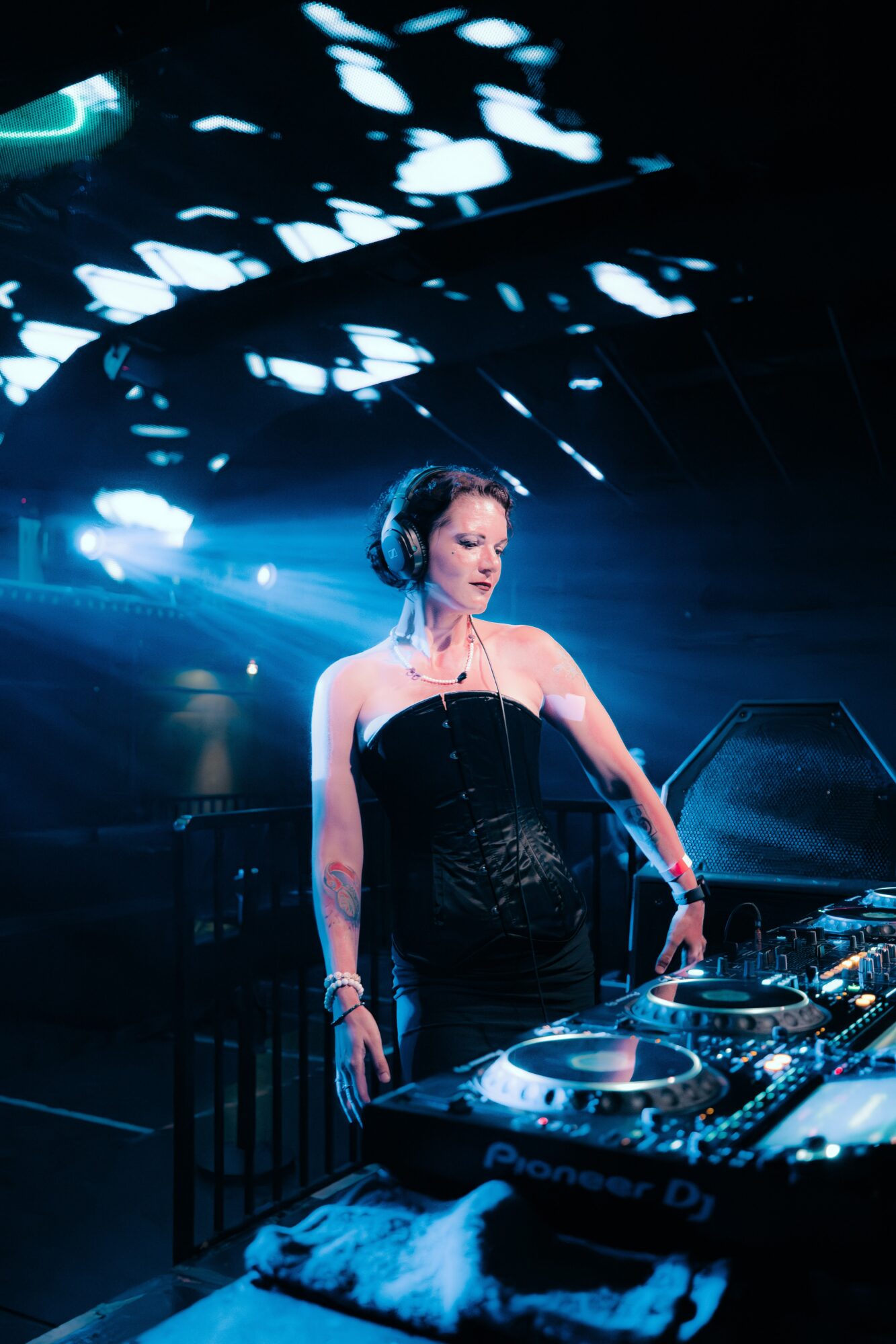 Female DJ wearing headphones and a strapless black dress performs at a nightclub with blue lighting.